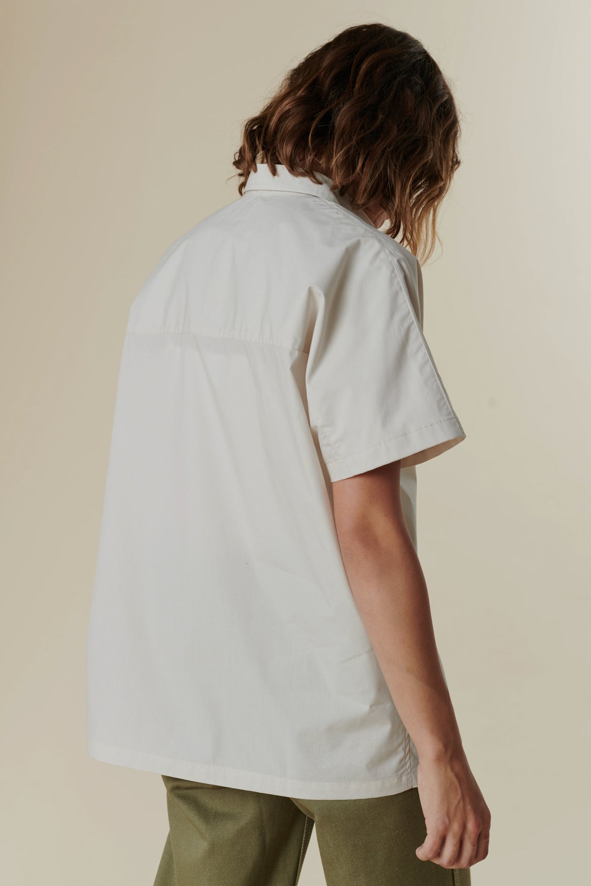 
            Back of a woman wearing the white Ava shirt on top of the Olive combat pant