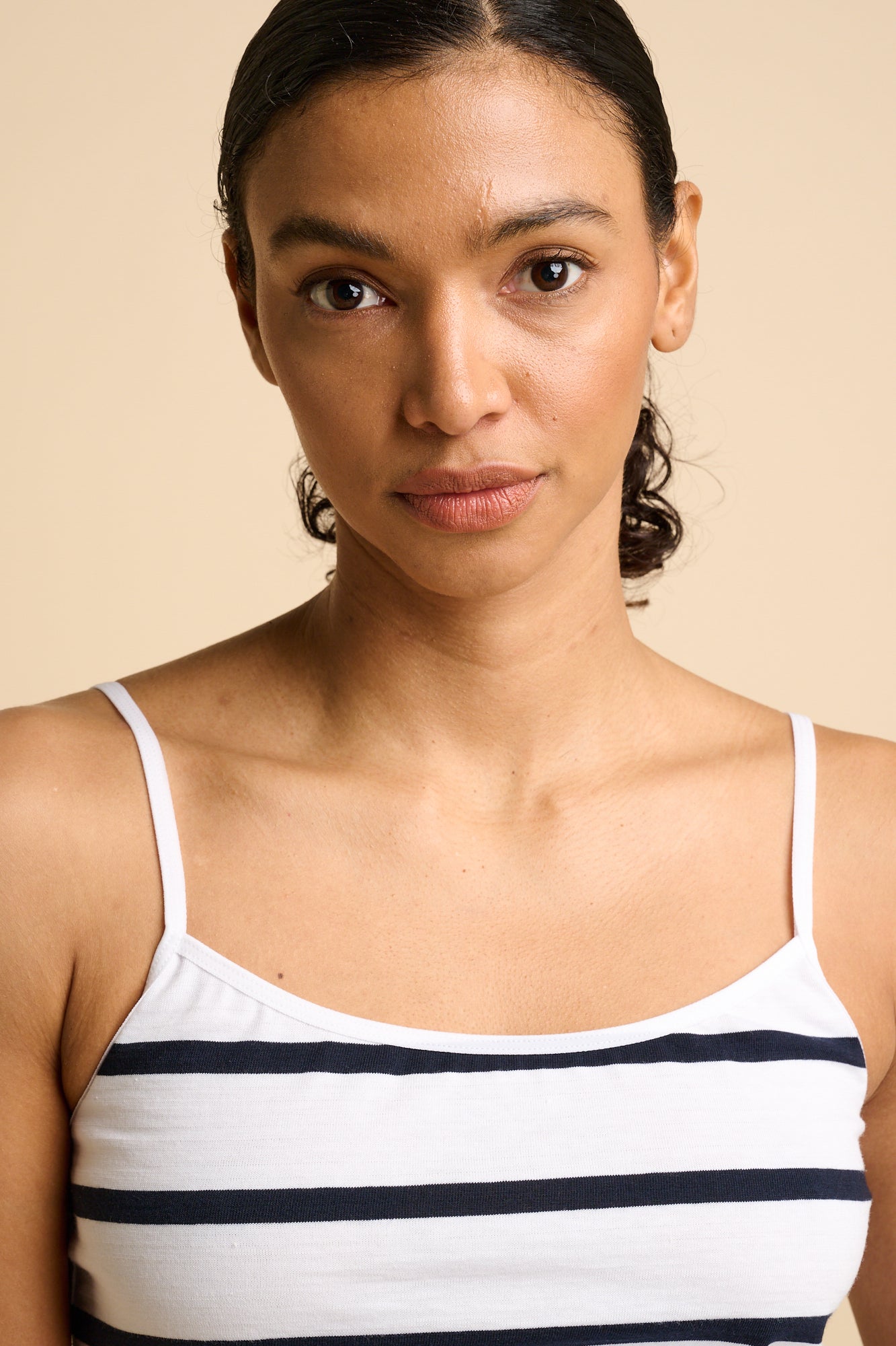 Woman wearing a striped camisole and denim shorts on a beige background