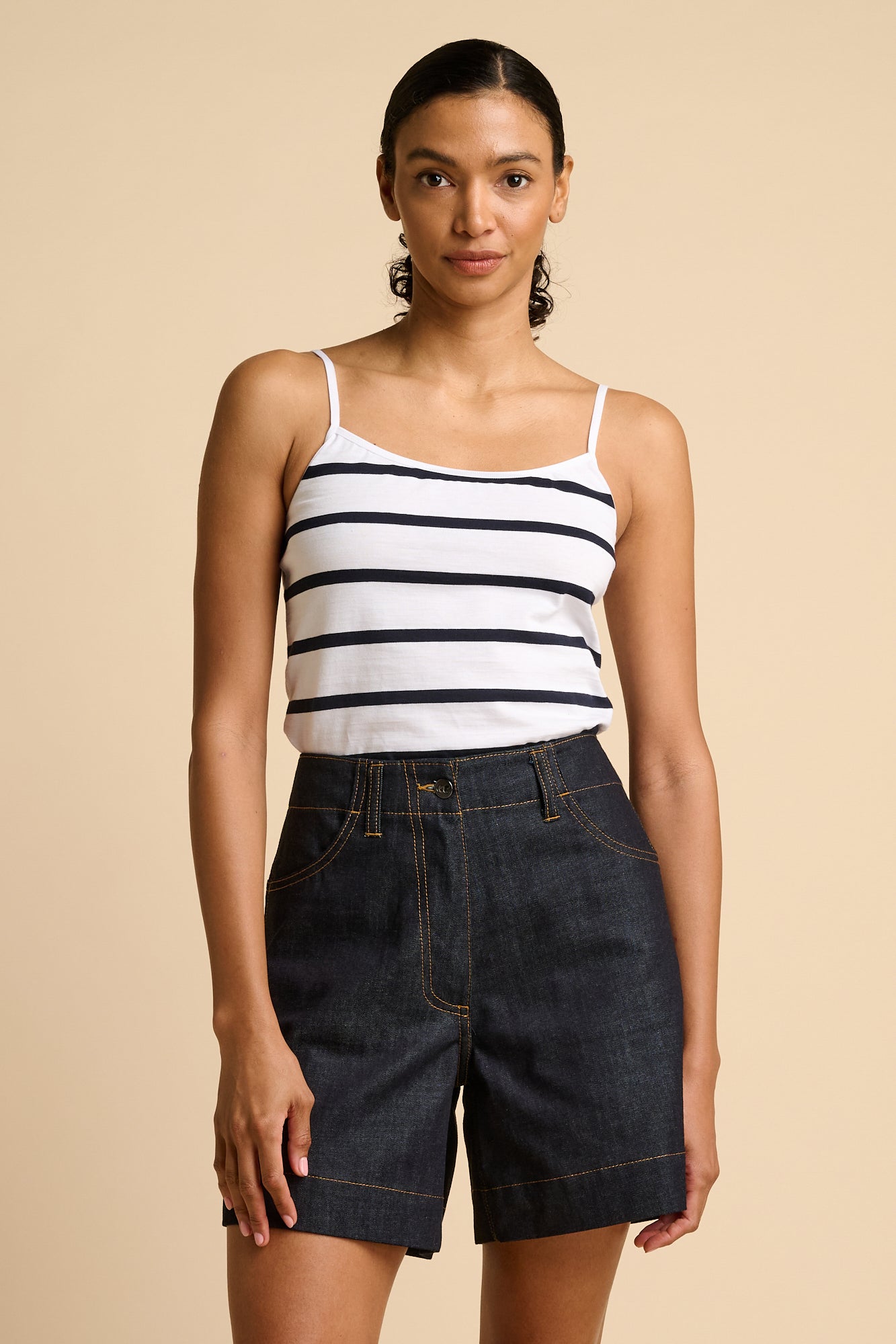 Woman wearing a striped camisole and denim shorts on a beige background