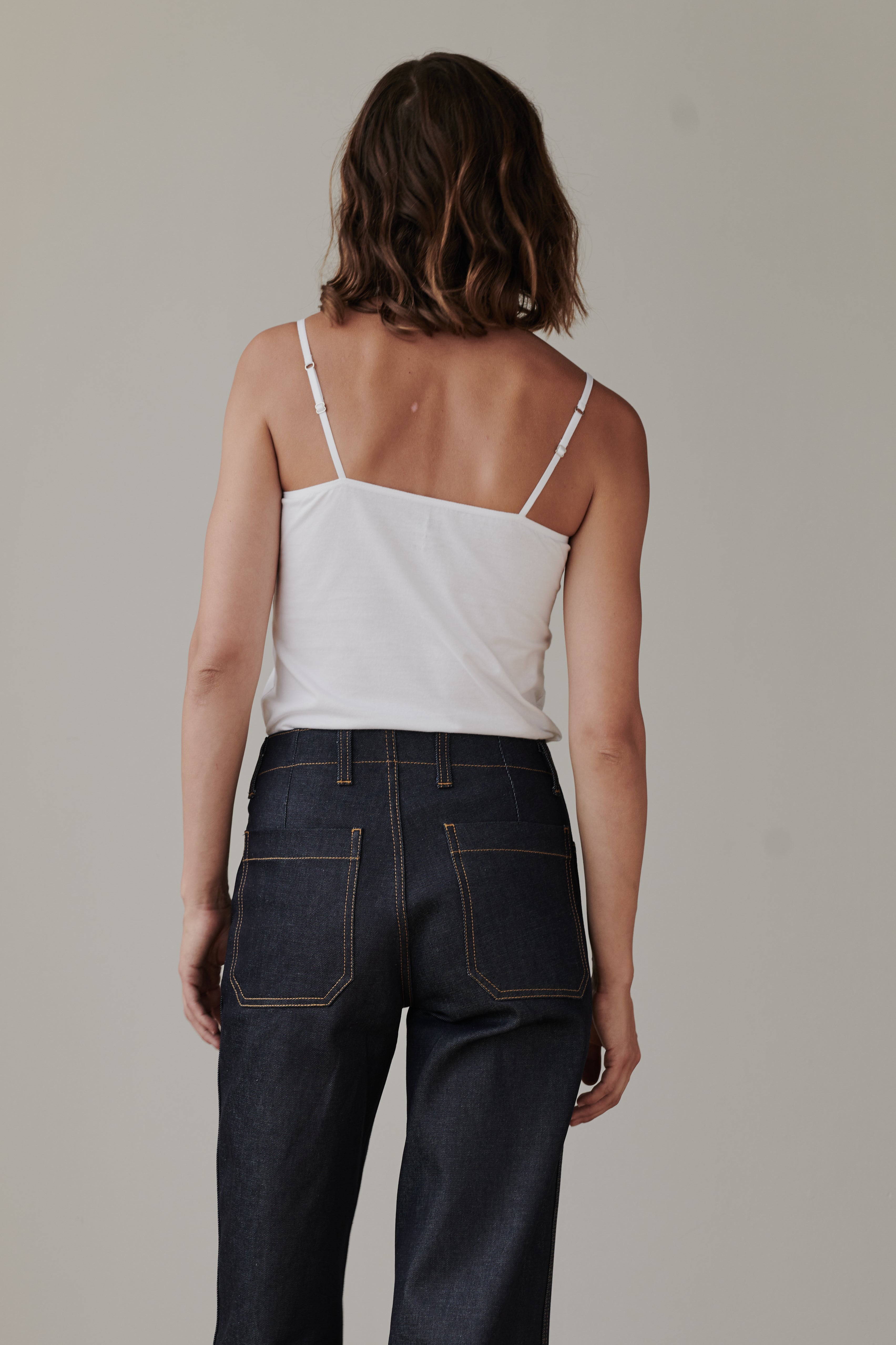 The back of female wearing camisole in white tucked into work jeans in indigo