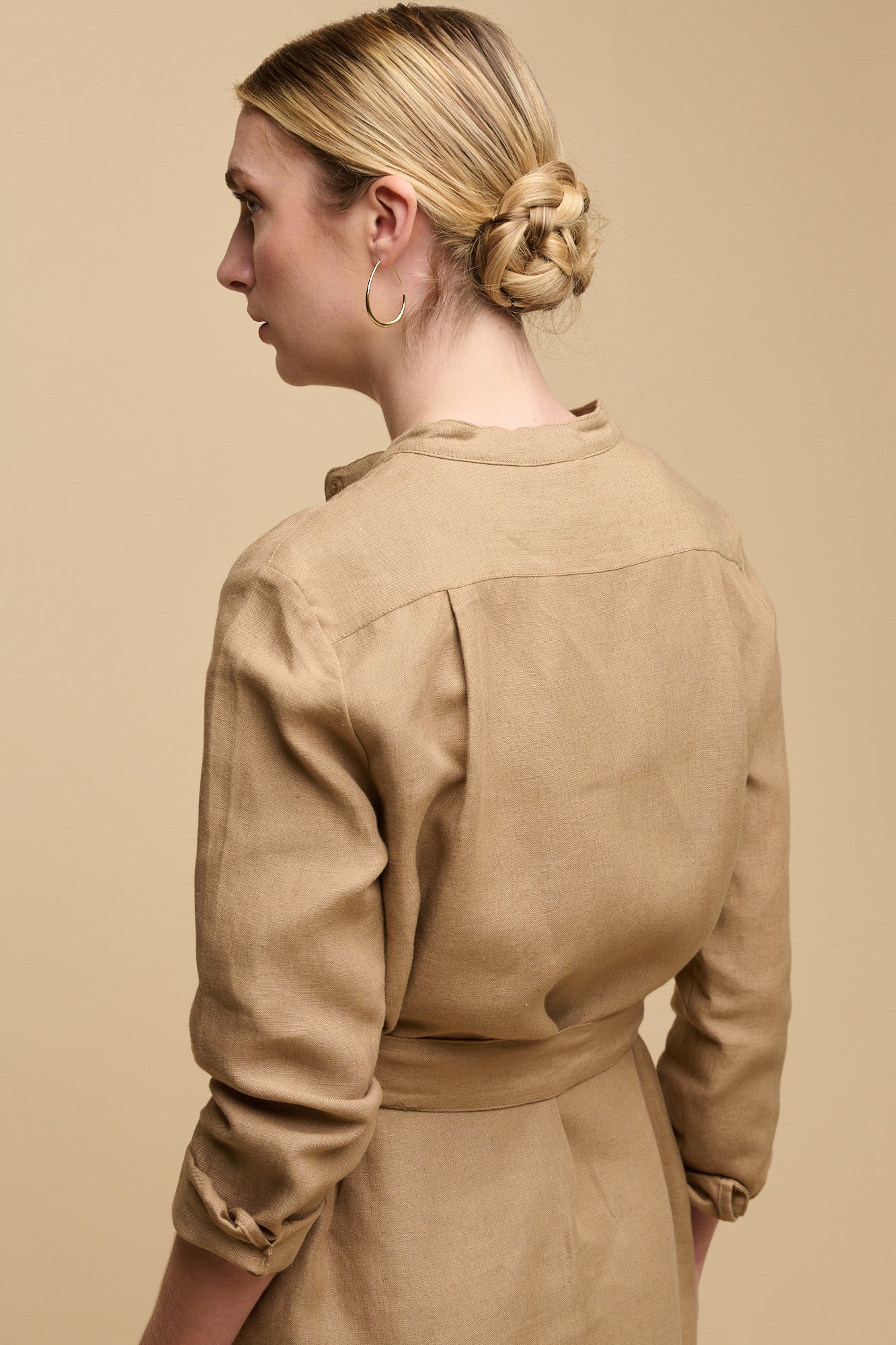 Hip up image of the back of collarless shirt dress in truffle linen, sleeves rolled up to below elbow.