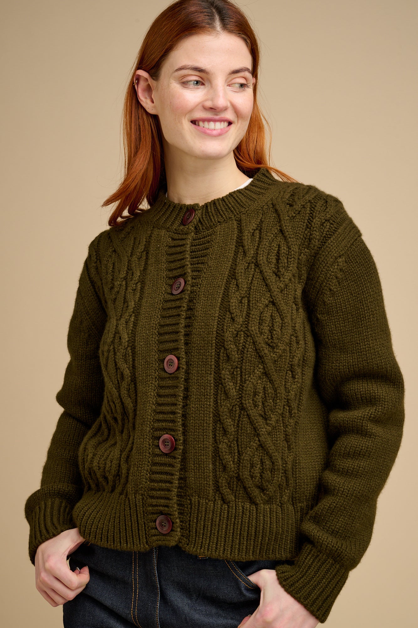 Woman wearing a green cable knit cardigan against a beige background