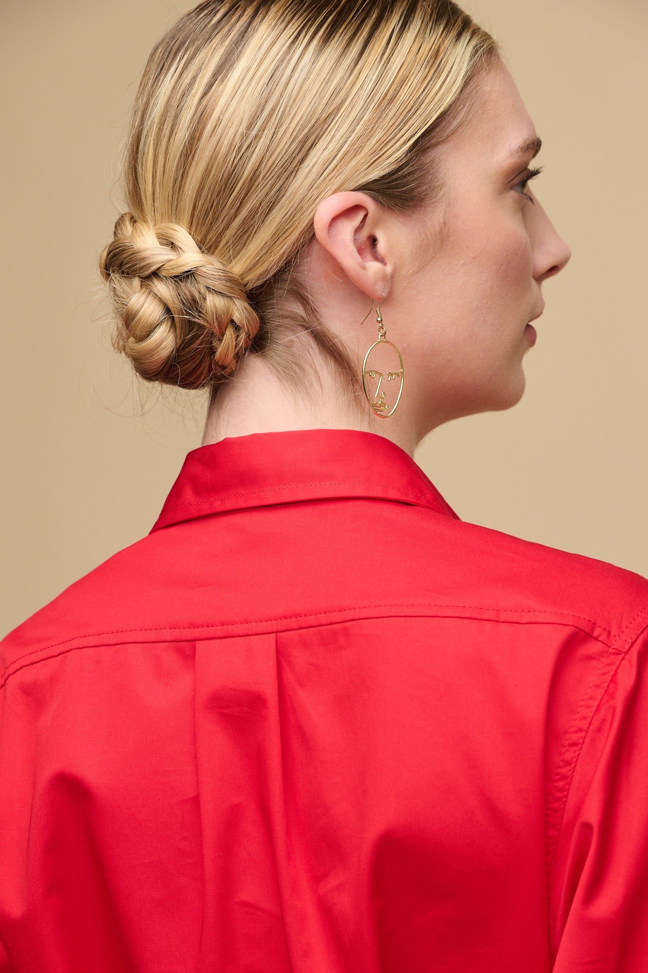 Close up of the back of female's shoulders wearing cotton dress in red, with hair in bun and detail gold earrings