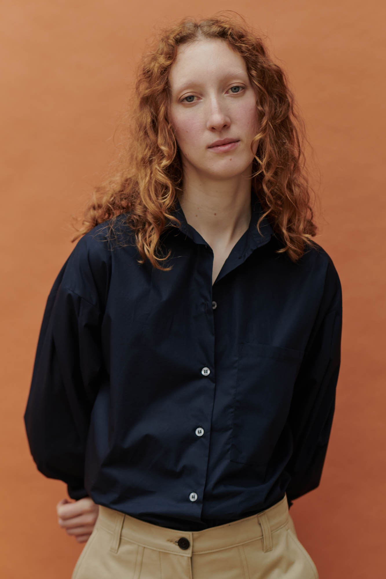 Female wearing the navy long sleeve shirt with the combat pant in front of an orange background.