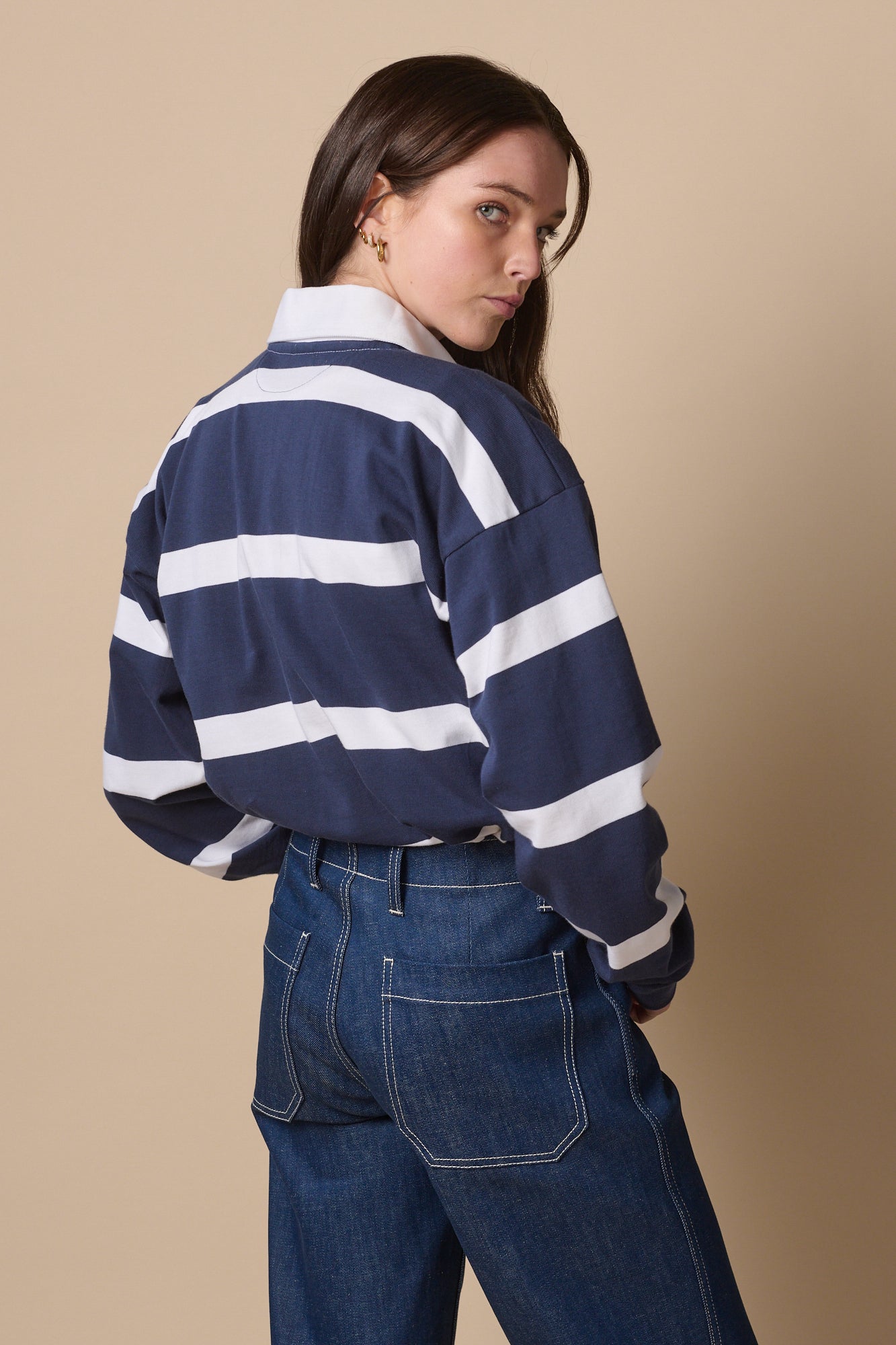 Female wearing fine stripe rugby shirt in navy white turned away, looking back to camera