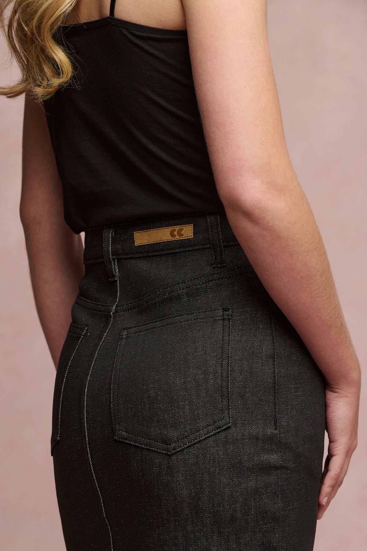 
            Close up of the back of female wearing Frankie denim maxi skirt in black with belt loops and two back pockets. Brown CC logo Jean patch on waistband 