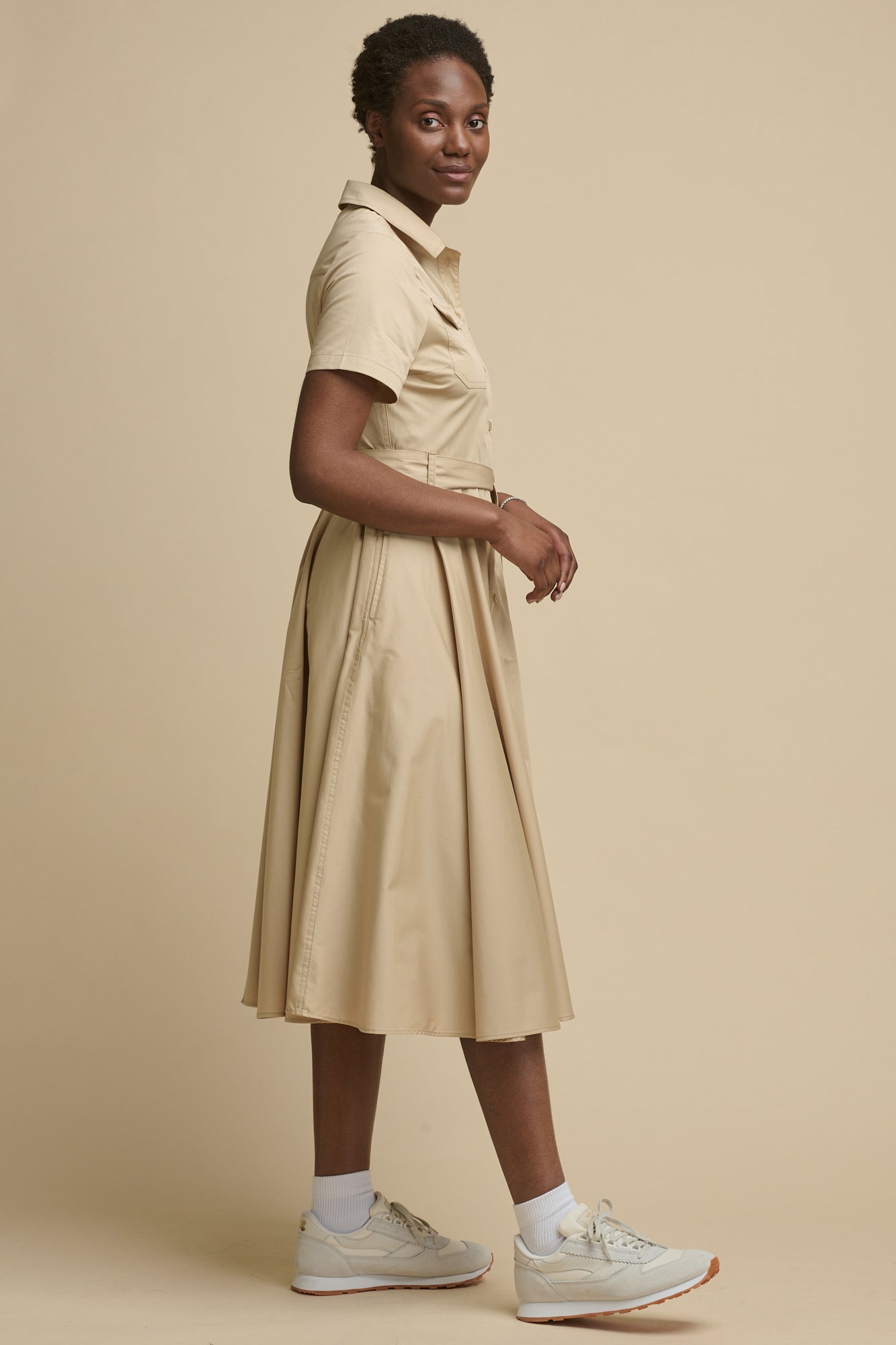 The side of female wearing full skirted phoebe trench dress in stone