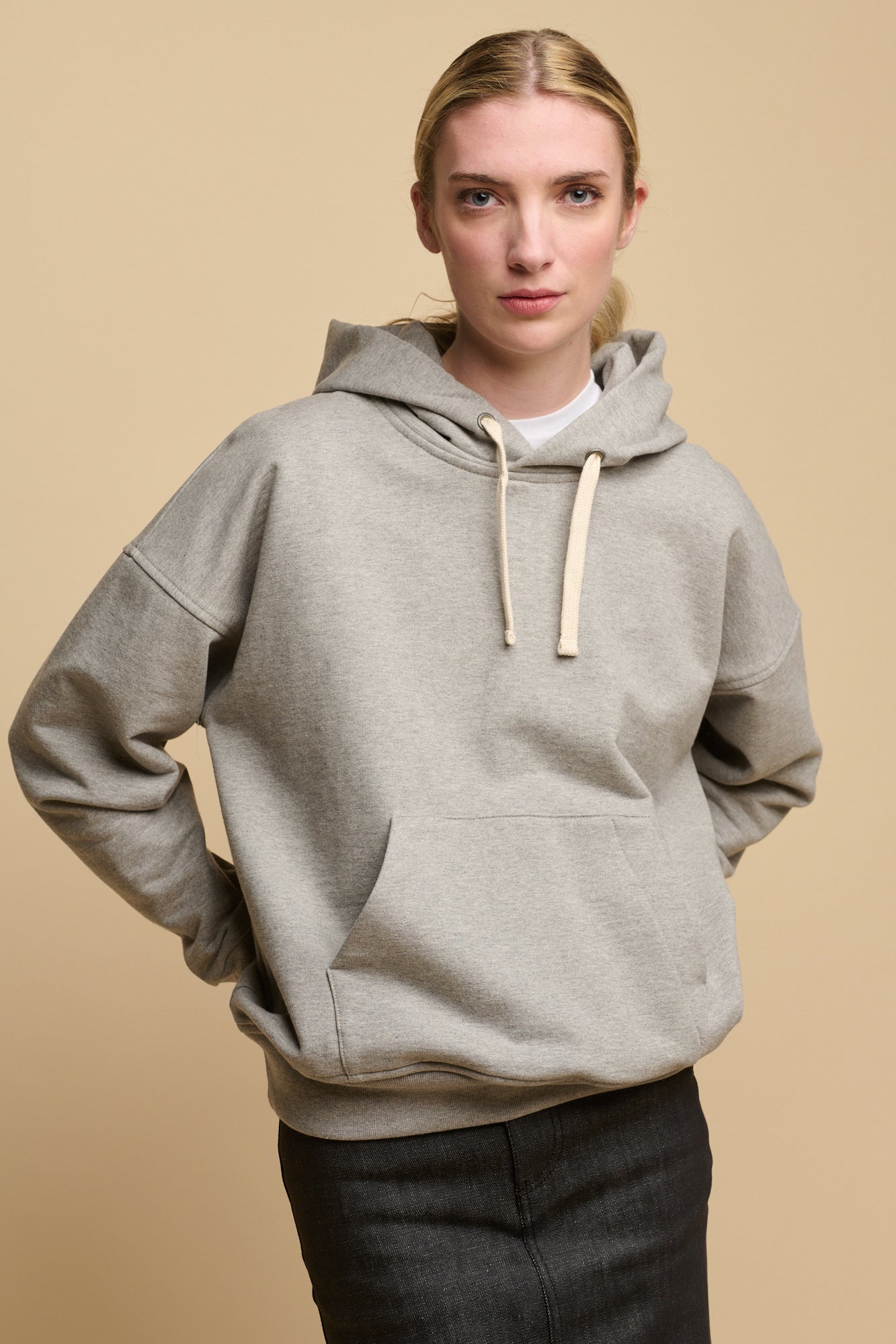 Female with blonde hair wearing heritage hooded sweatshirt in grey with ecru drawstring through the hood. worn over crew neck white t shirt in white