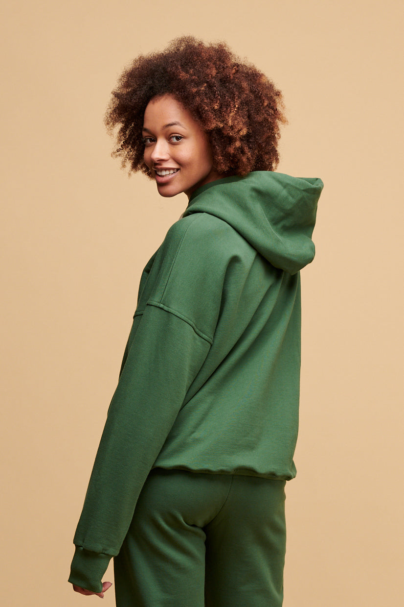 Thigh up of the back of female looking back to the camera wearing hooded sweatshirt in bottle green