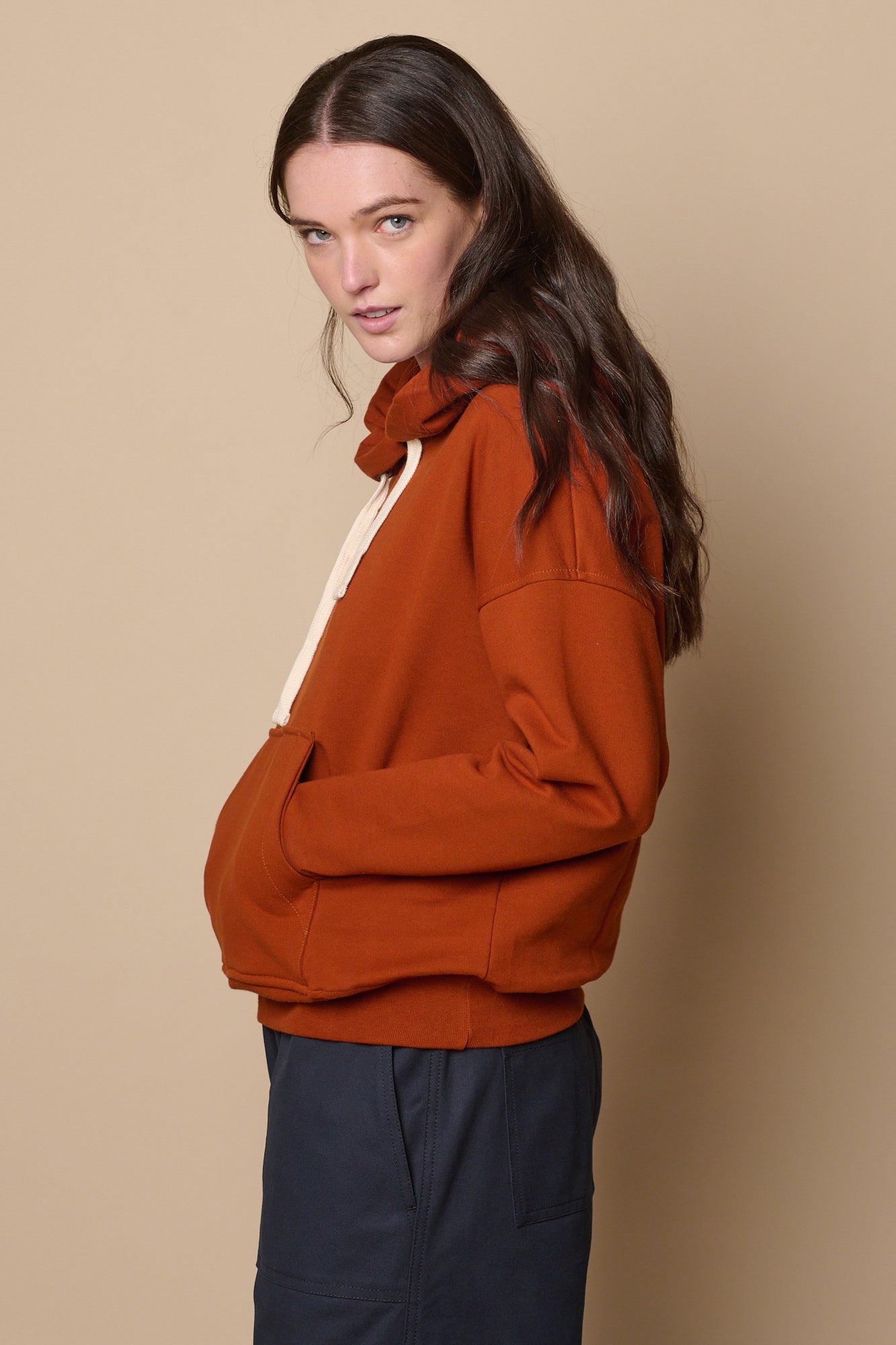 Thigh up image of the side of hooded sweatshirt in cinnamon, hands in front pocket