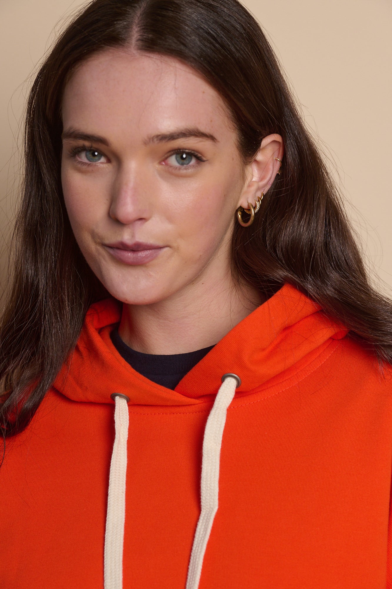 Portrait of female wearing hooded sweatshirt in flame red with drawcord through the hood, navy t shirt worn underneath.