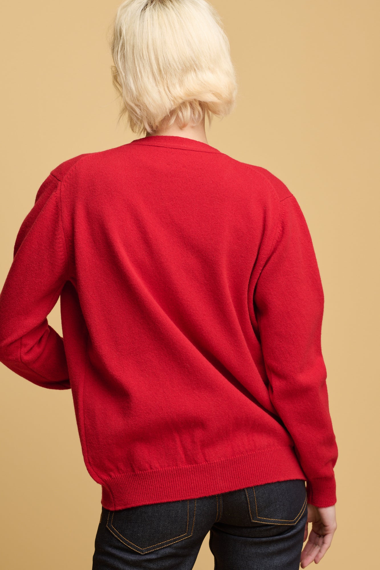 Thigh up of the back of female wearing lambswool cardigan in red with indigo jeans