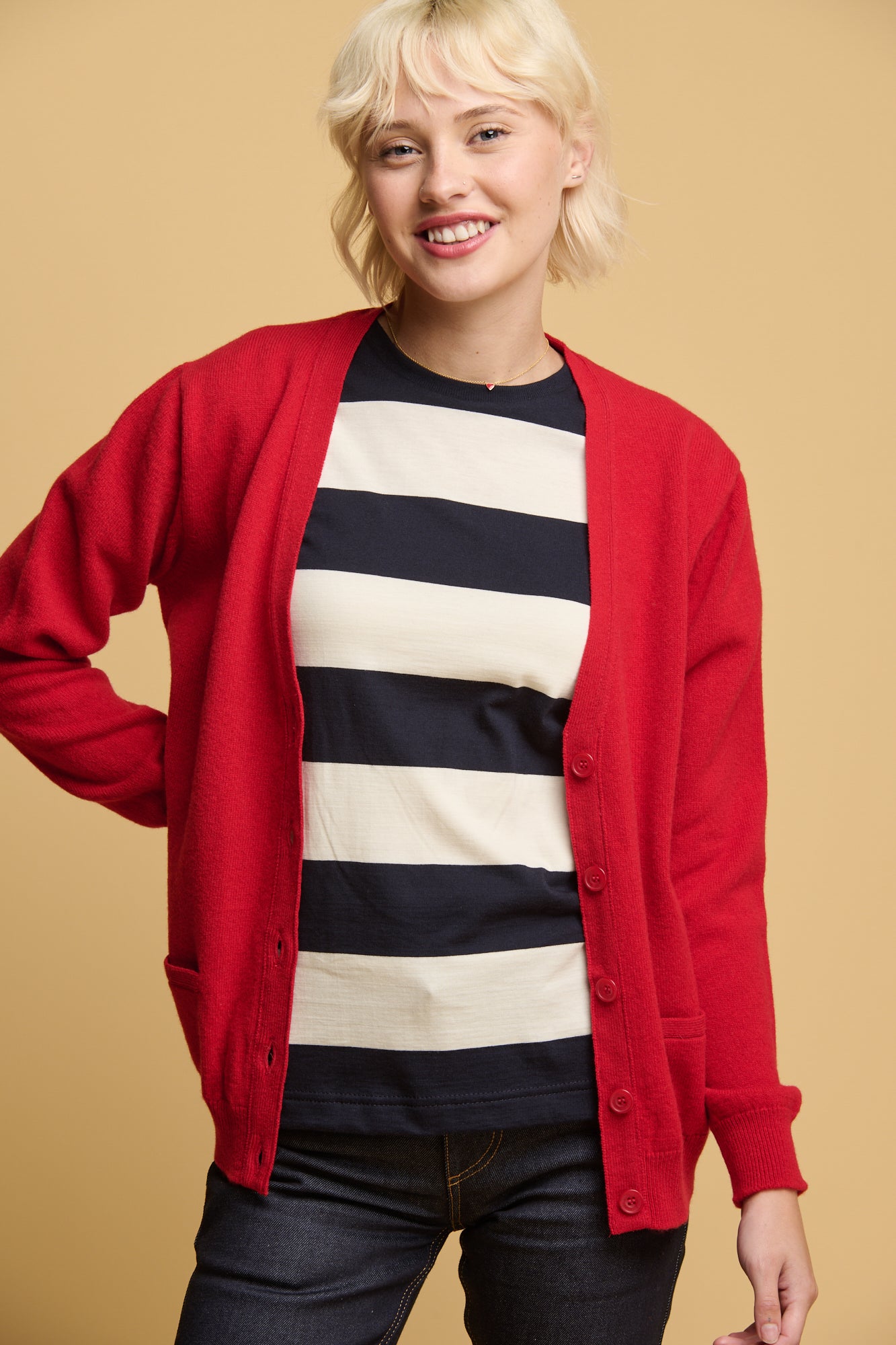 Thigh up front of female wearing v neck cardigan in red unbuttoned over wide stripe t shirt in ecru and navy