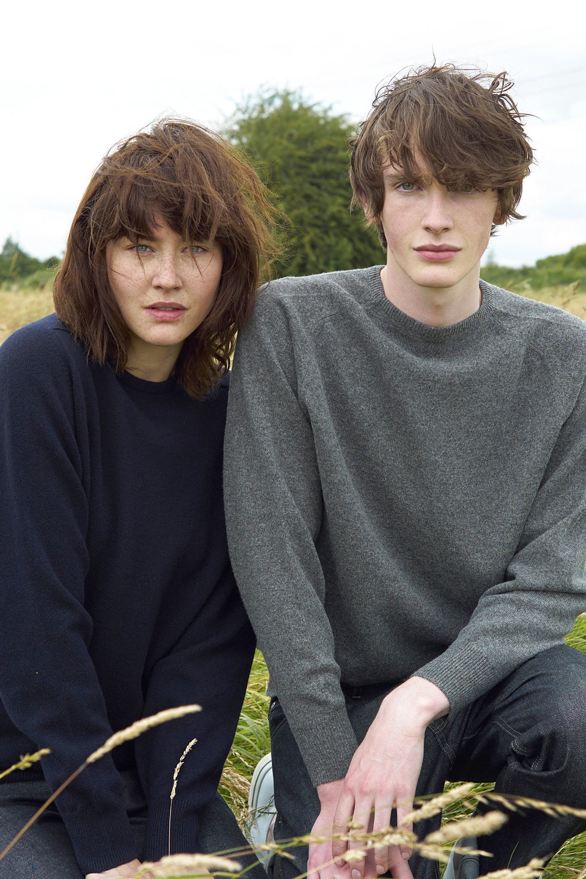 
            Male and female posing outside in field in lambswool crew neck jumpers, female wearing navy and male wearing grey