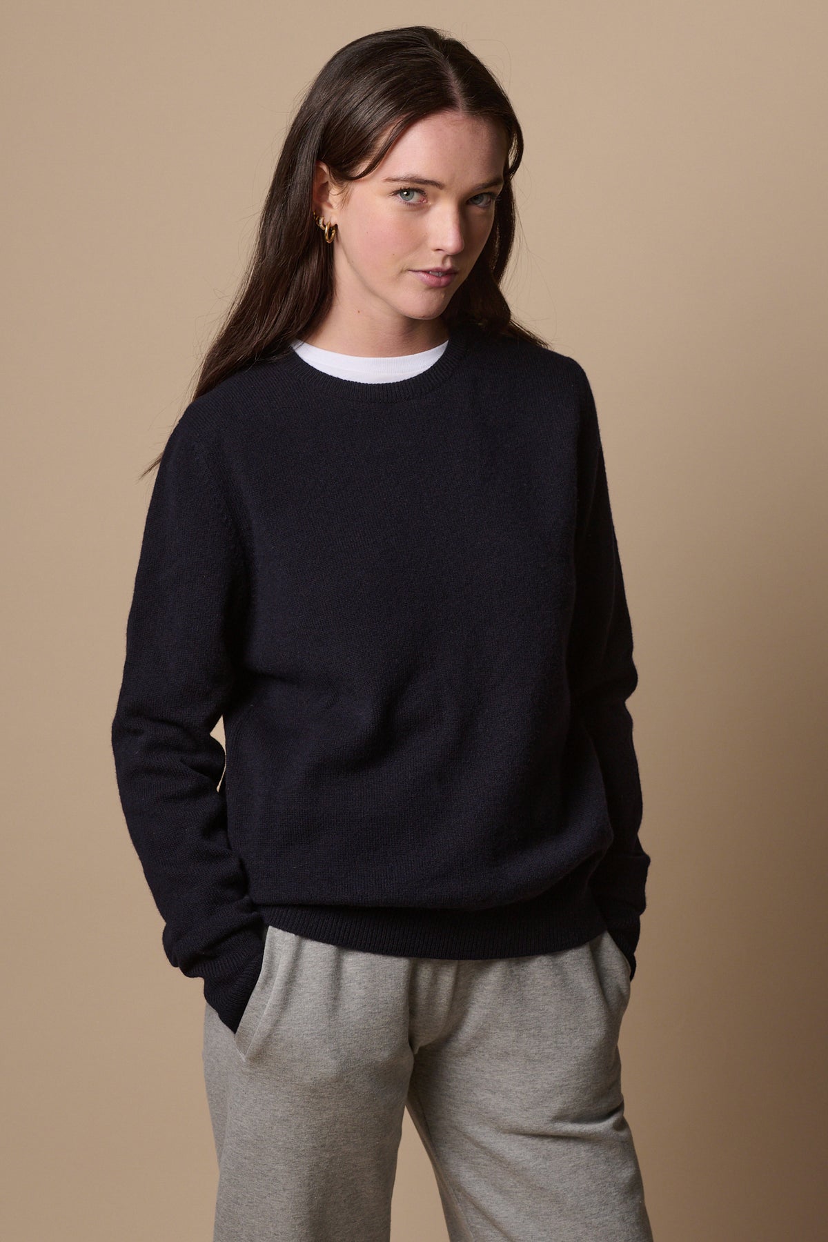
            Brunette female wearing lambswool crew neck jumper in navy layered over white t shirt and worn with sweatpants in grey marl