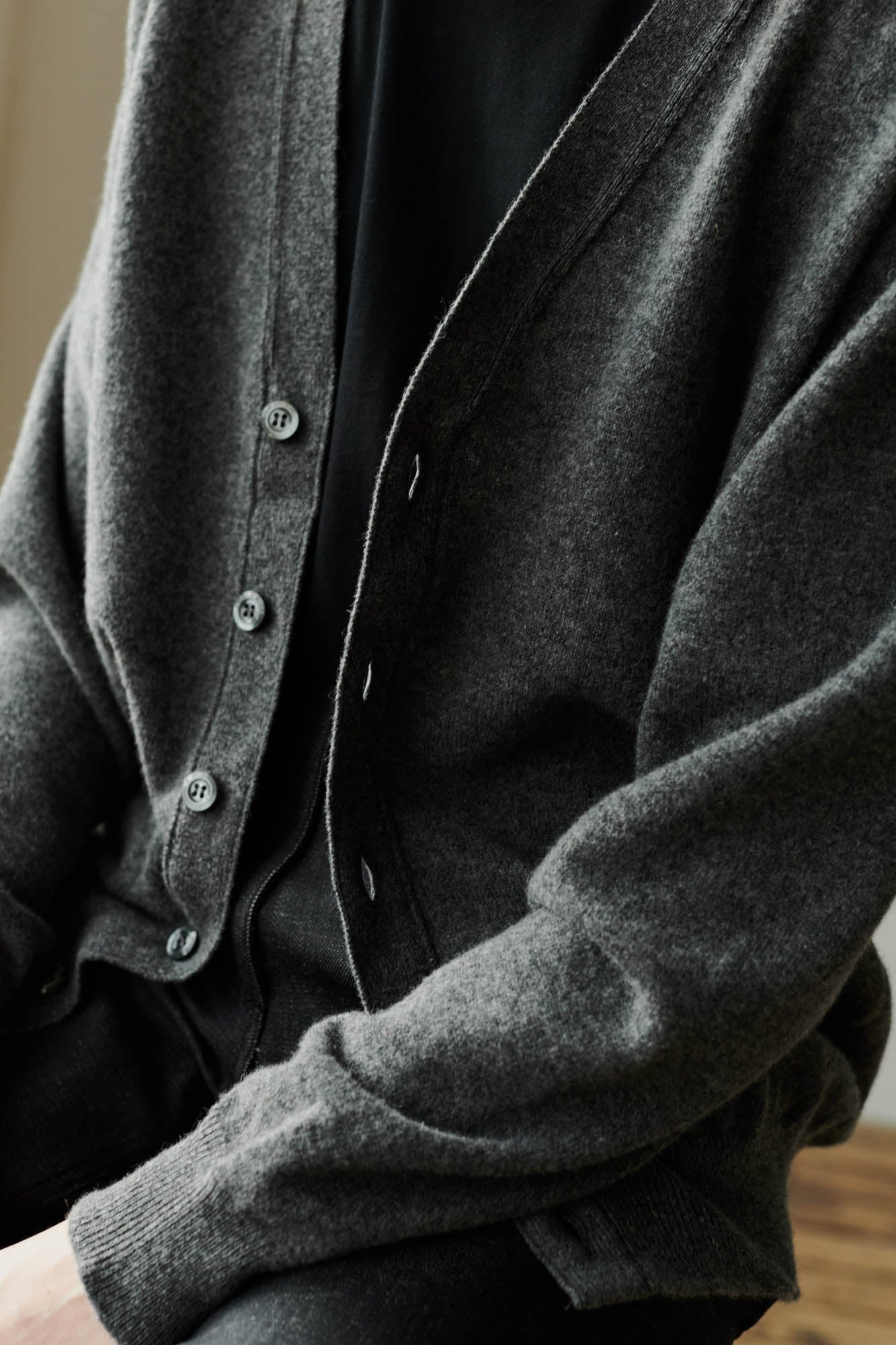 Button fastening detail and ribbed cuff close up of female wearing lambswool v neck cardigan in charcoal