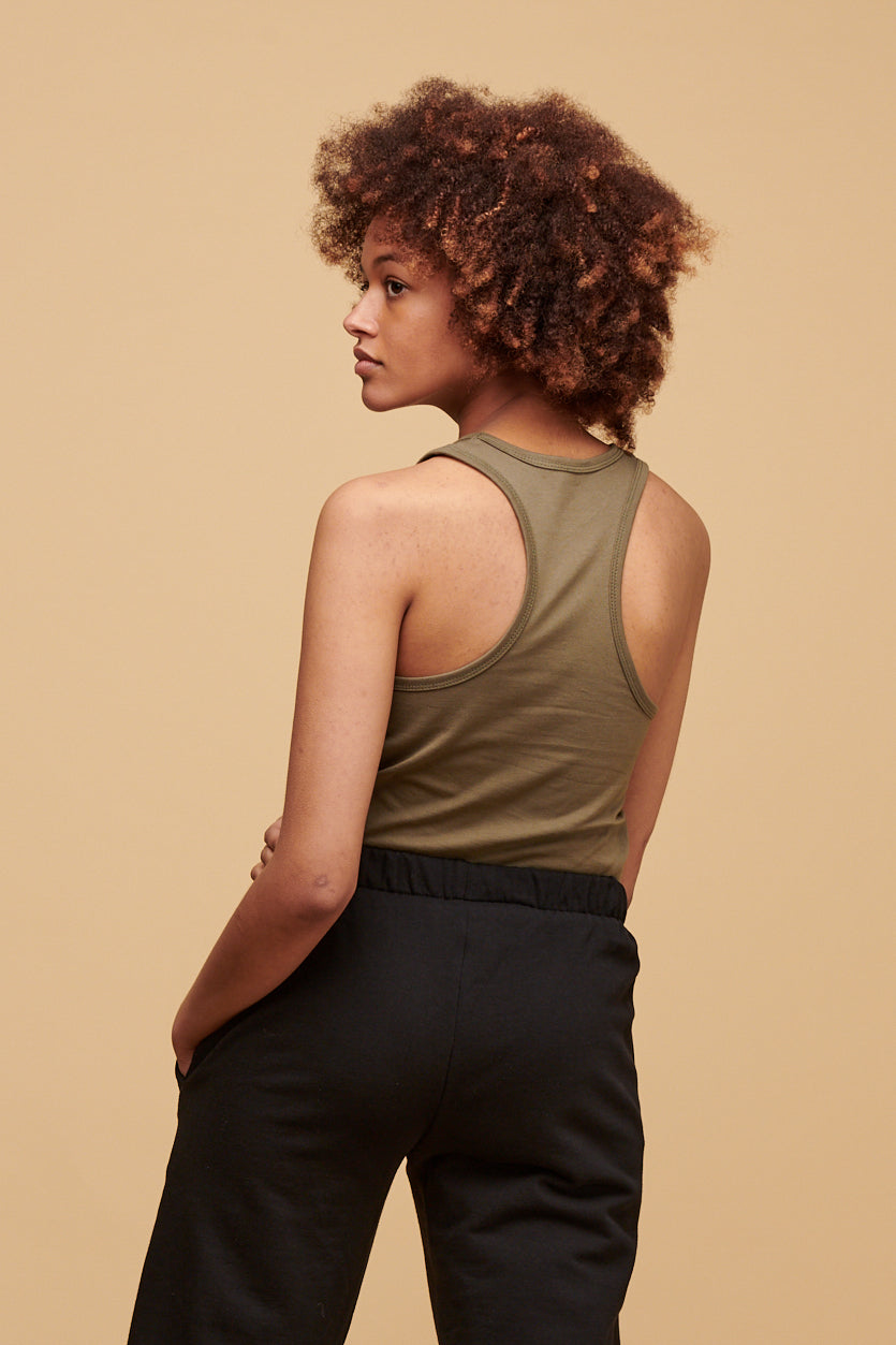 Thigh up of the back of female wearing racer back vest in olive tucked into sweatpants in black