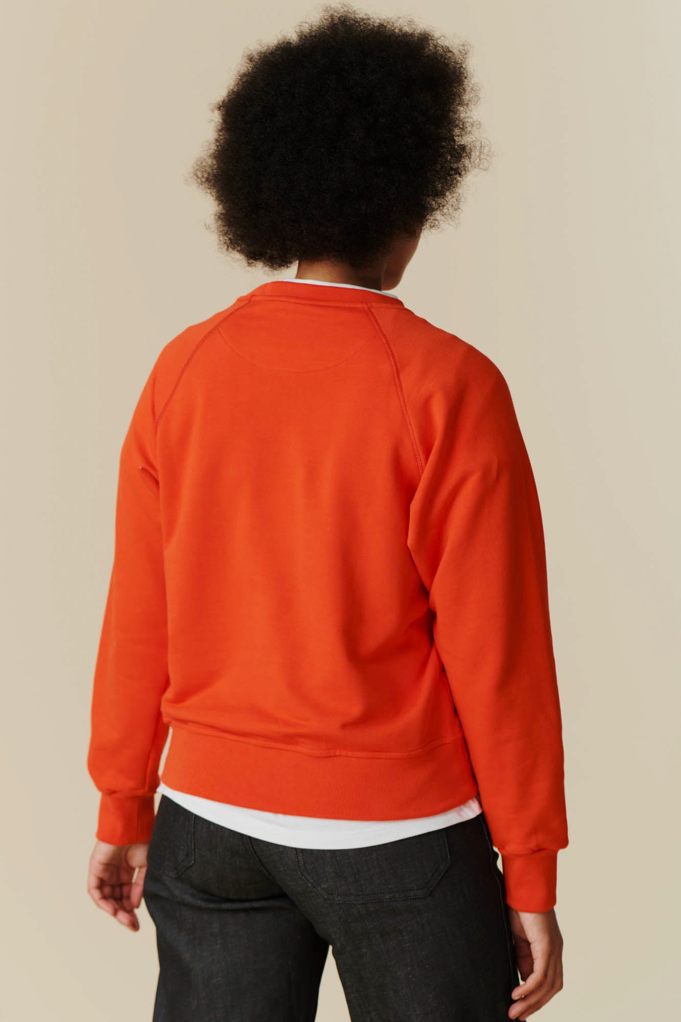 Back of female in women's raglan sweatshirt in flame red