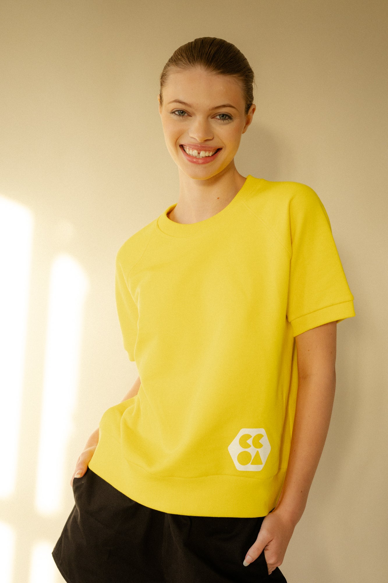 Smiley, white female wearing short sleeve raglan training top in Canary Yellow with white CCOA Logo.