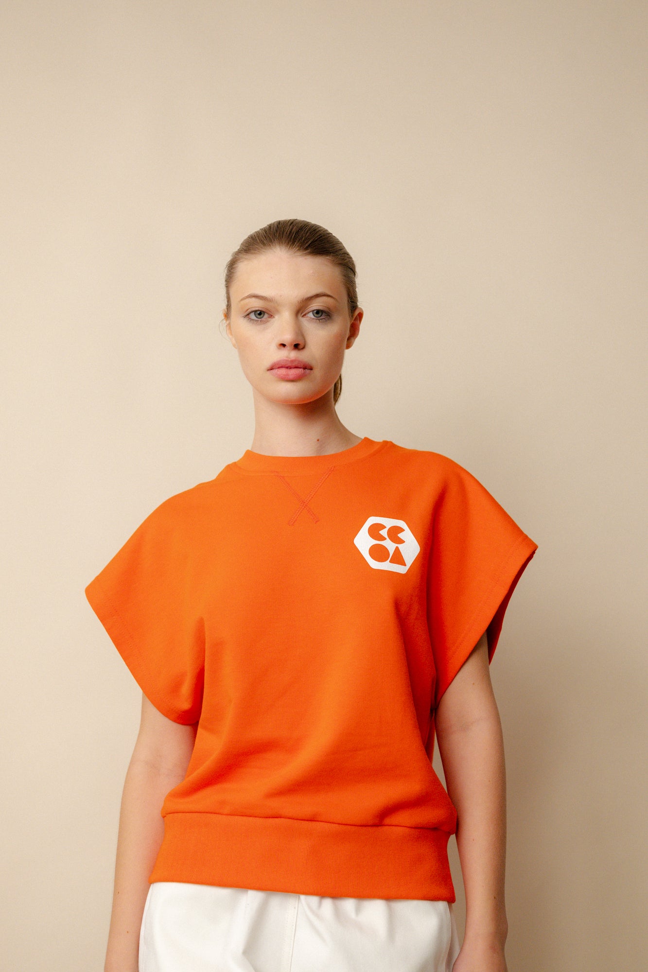 Hip up image of white, brunette female wearing sleeveless sweatshirt plastic free in flame red. White CCOA logo print