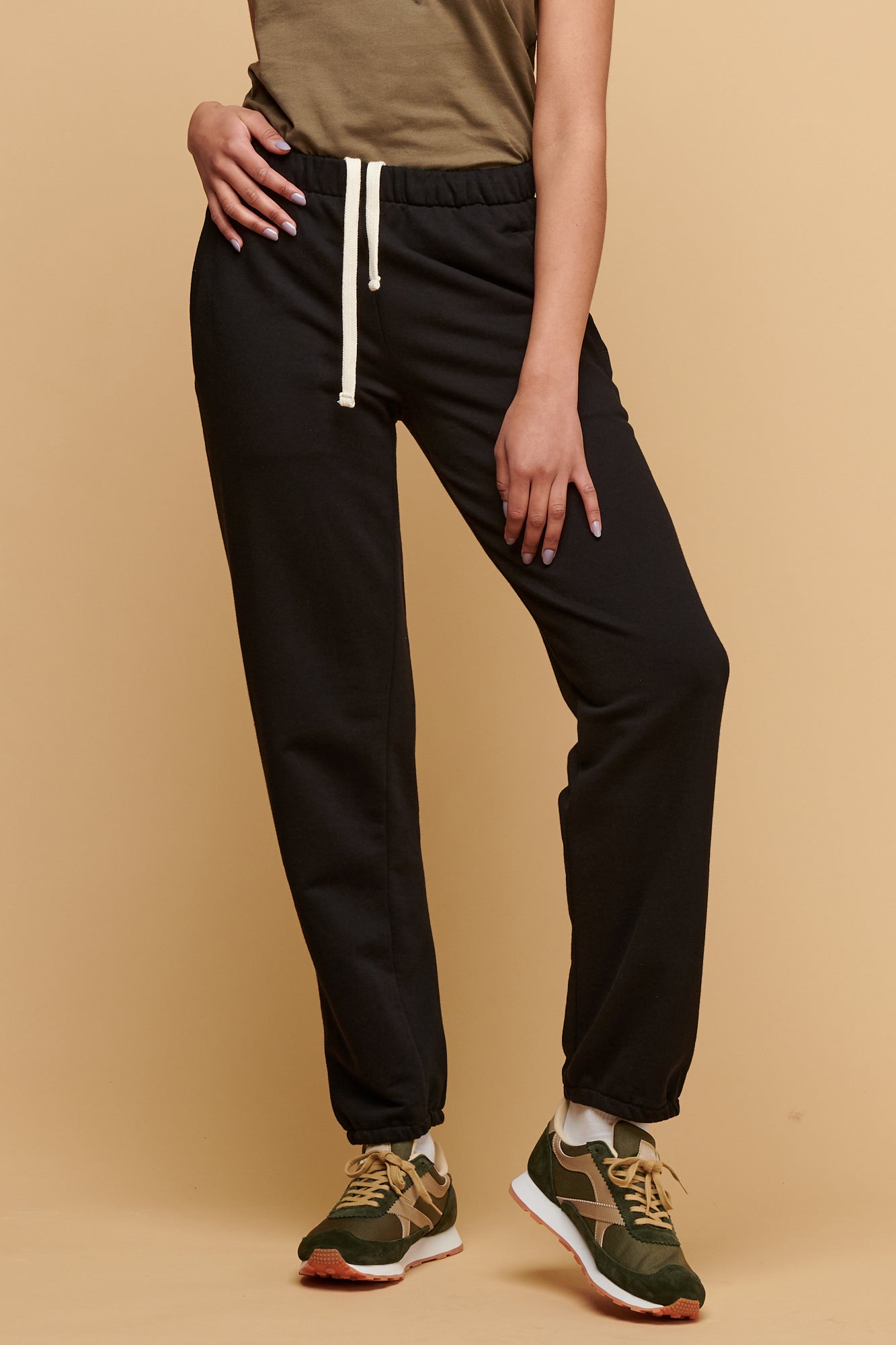 Chest down of female wearing 100% cotton sweatpants in black with ecru drawcord through the waistband paired with racer back vest tucked into joggers with Walsh Footwear X Community Clothing Beacon trainers in olive/Beige