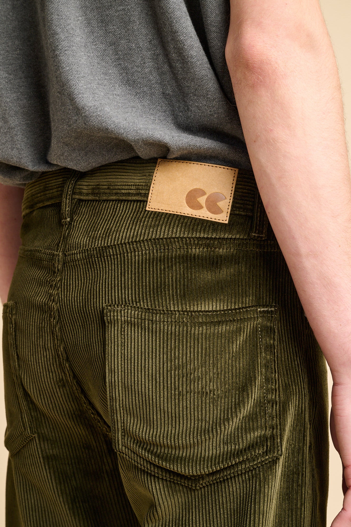 Close up of the back of male wearing dark olive corduroy jeans with CC logo jeans patch.