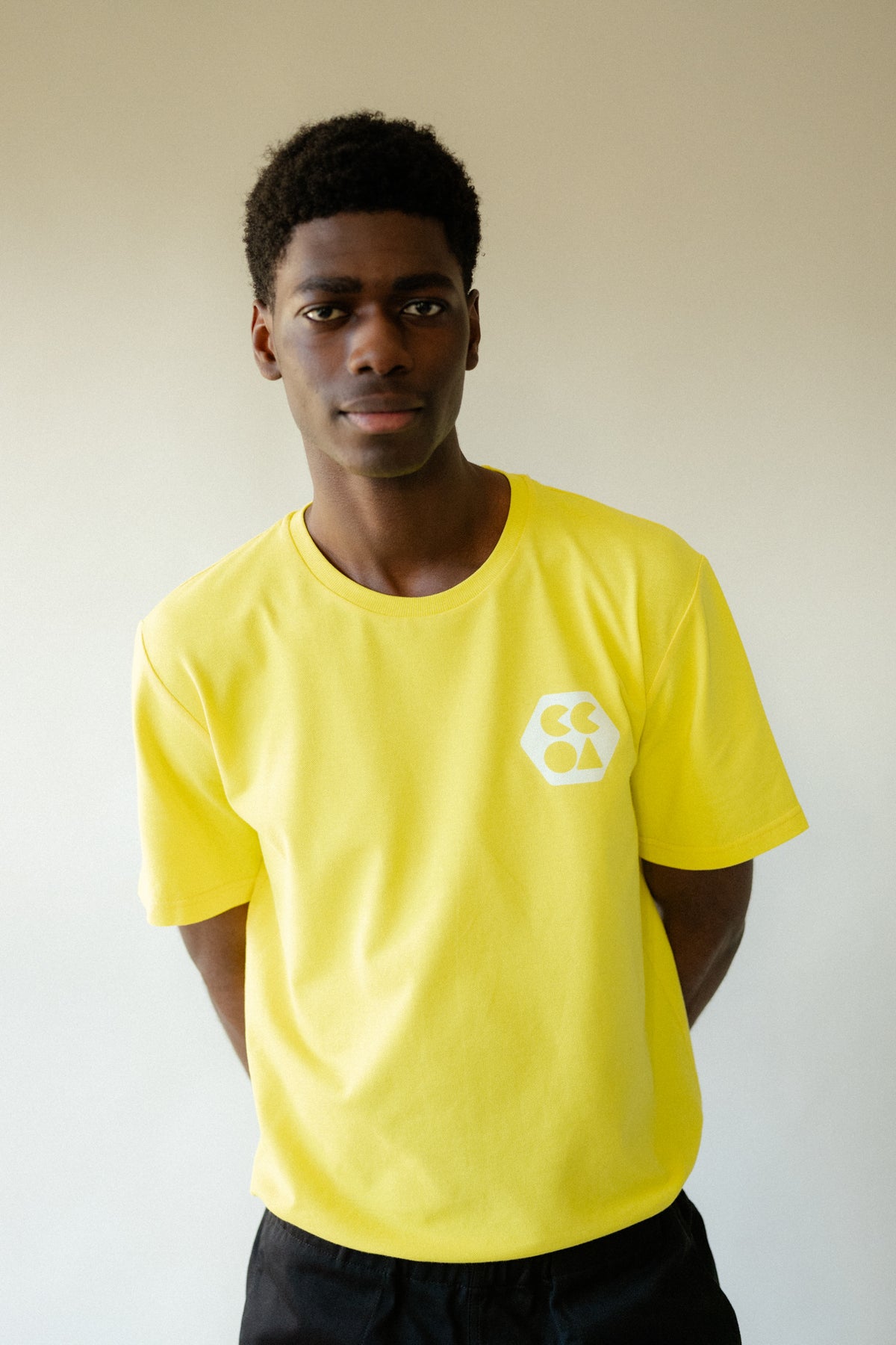 
            Male wearing men&#39;s breathable t-shirt plastic free in canary yellow with white CCOA logo