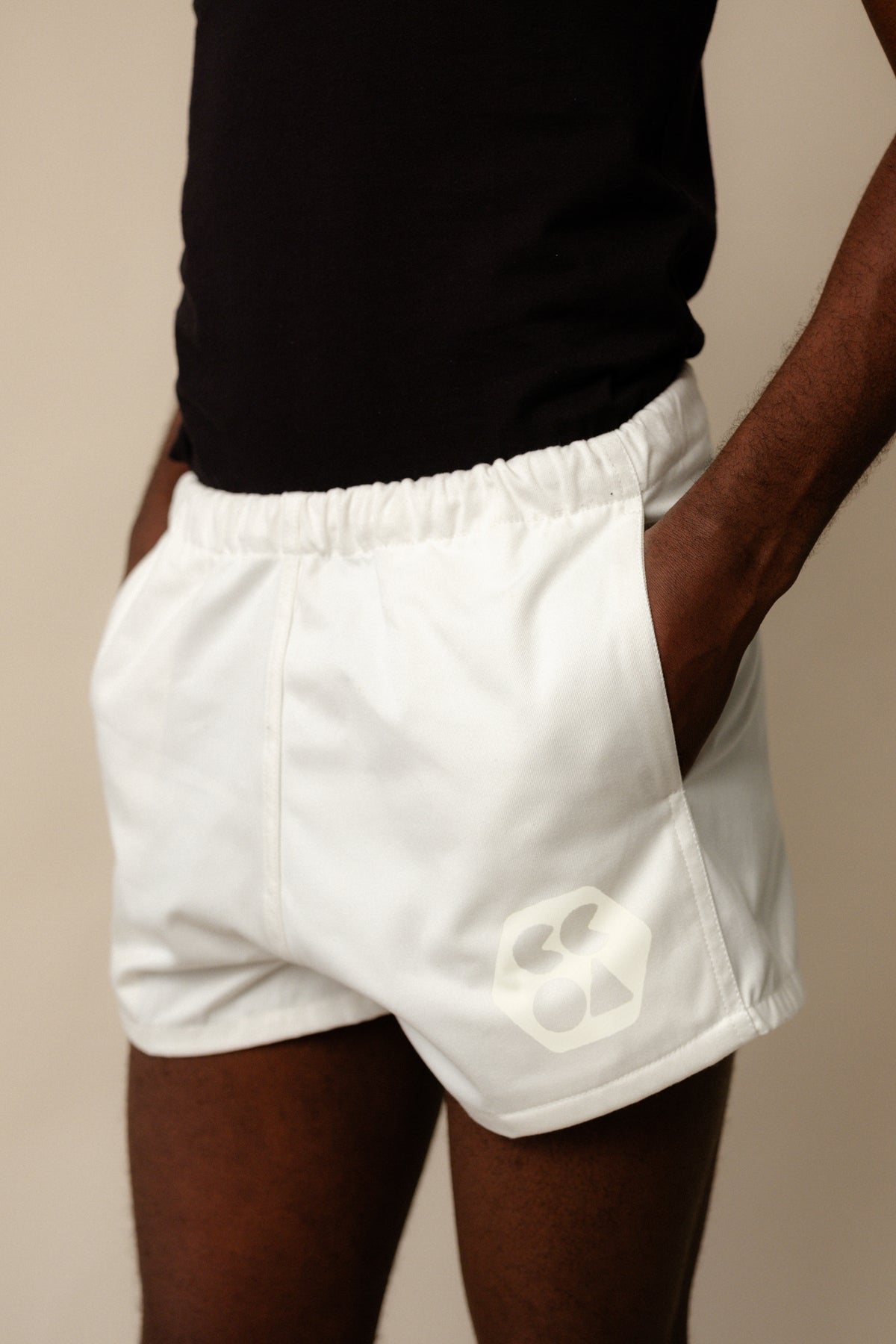 
            Male chest to knee wearing heavyweight sports short plastic free in white with CCOA logo, showing elasticated waistband and front pockets