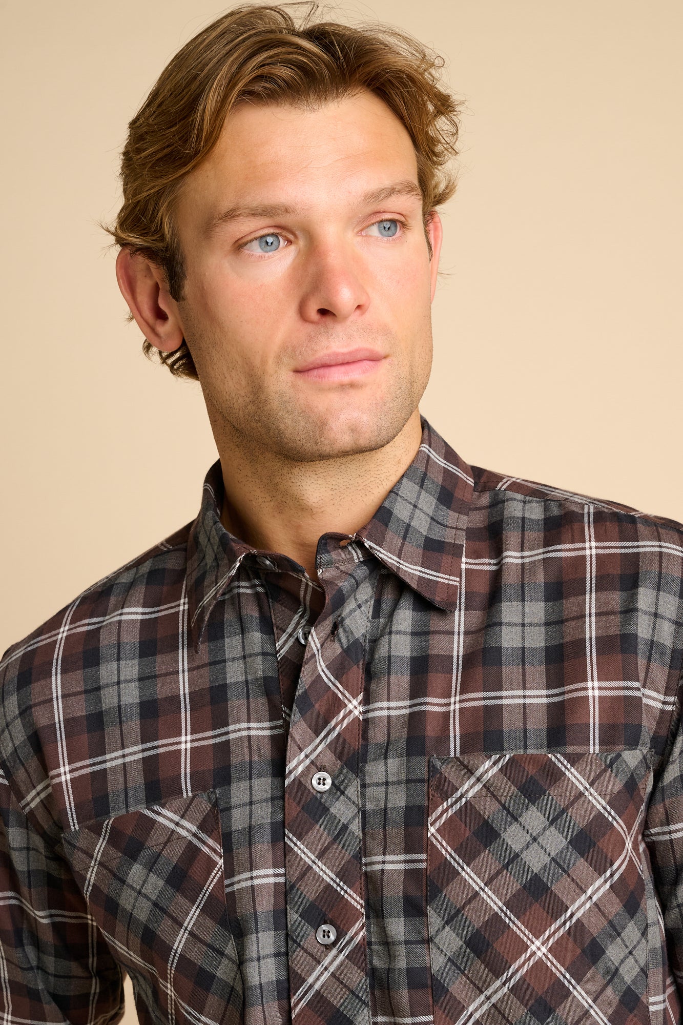 Man wearing check shirt against beieg background.