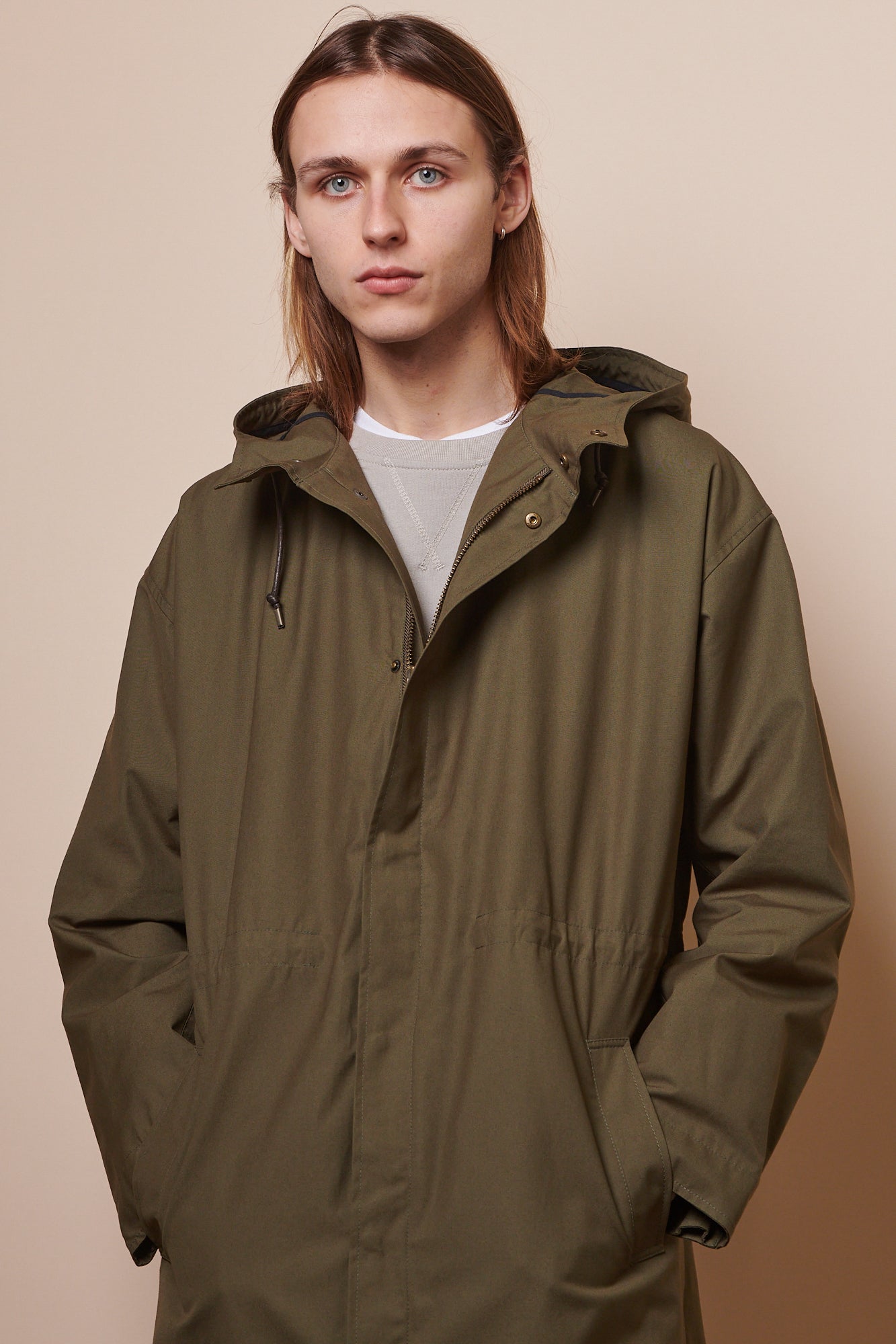 Thigh up image of male wearing parka in olive with hands in front pockets