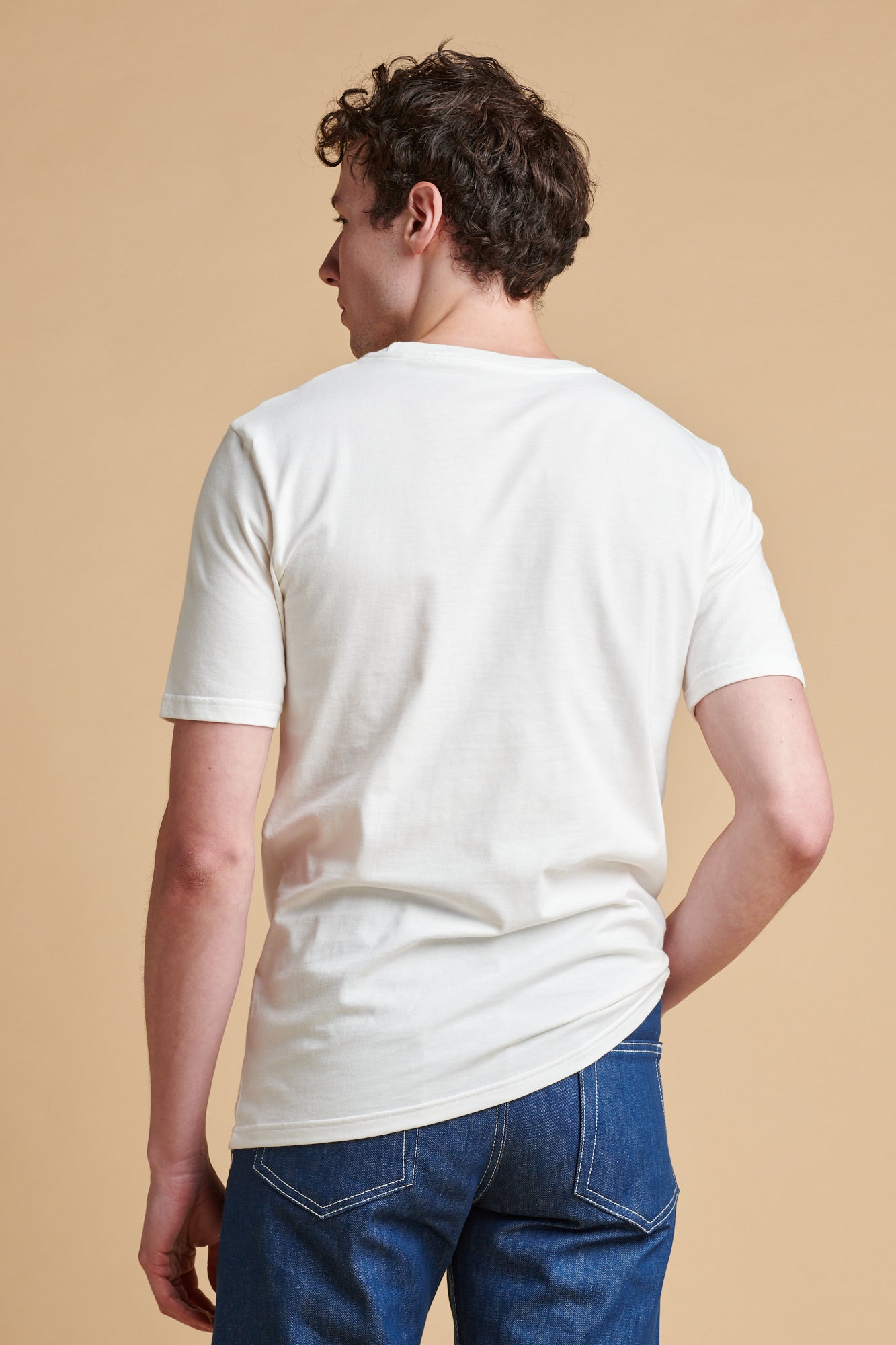 Man wearing a plain white t-shirt and blue jeans against a beige background