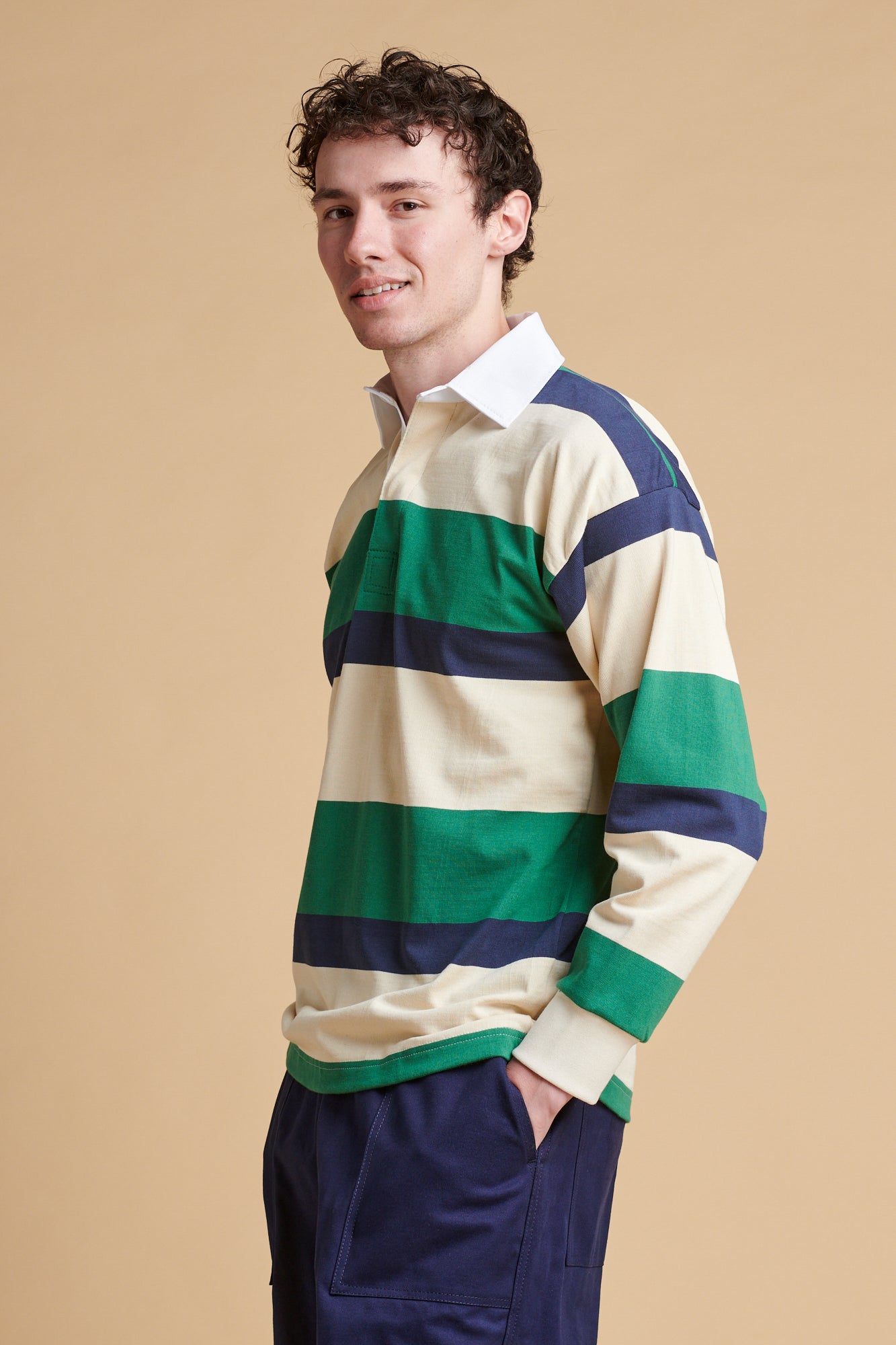 Male wearing striped rugby shirt in ecru navy bottle green.