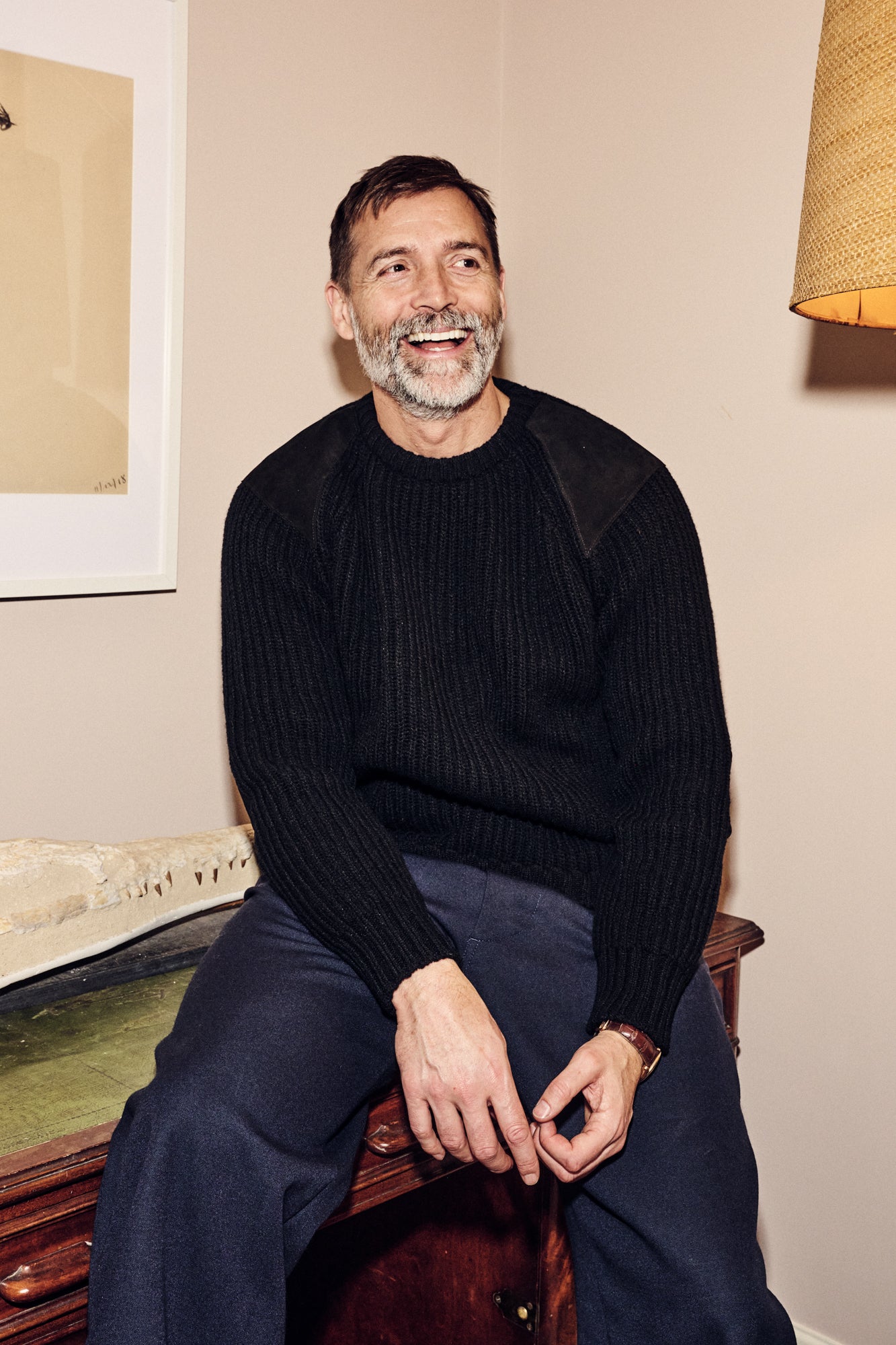Patrick Grant sat of side board wearing lambswool fisherman ribbed jumper in black.