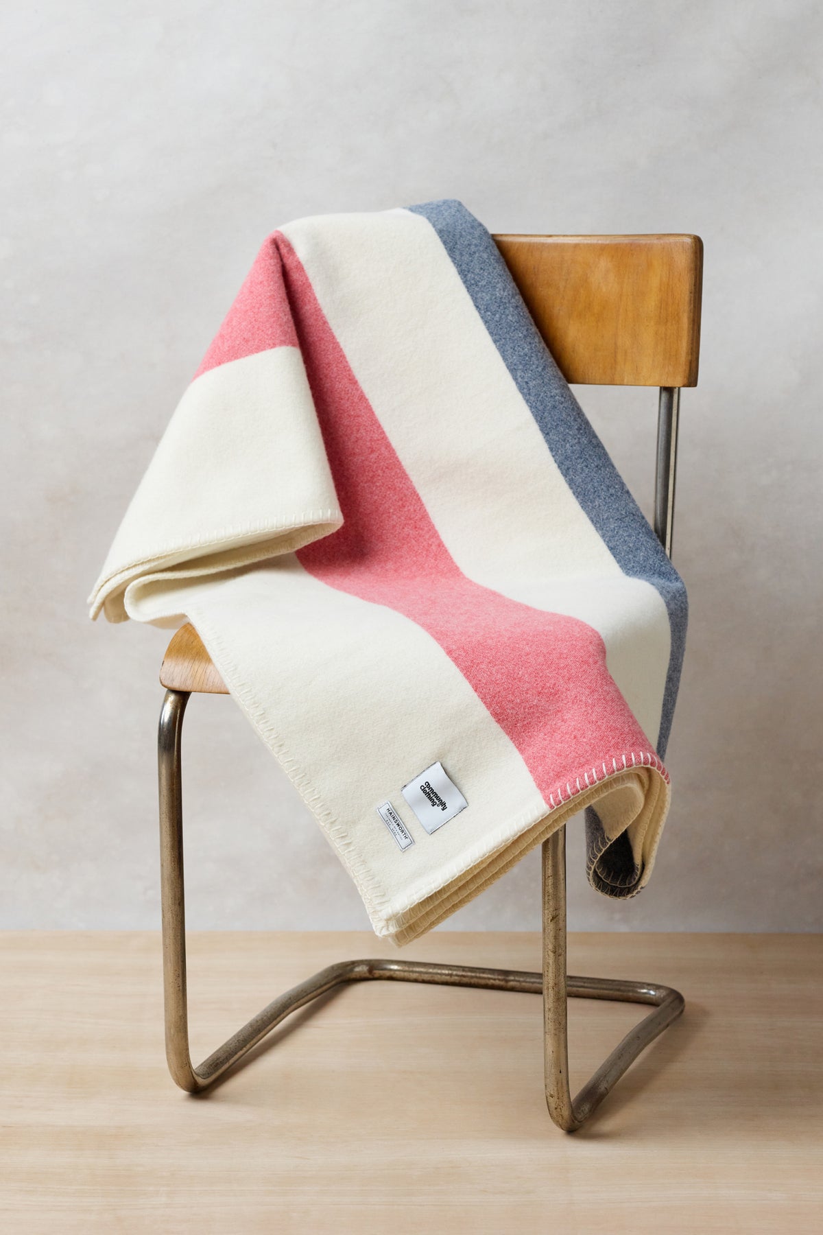 
            Folded pure wool striped blanket in ecru red navy draped over vintage chair