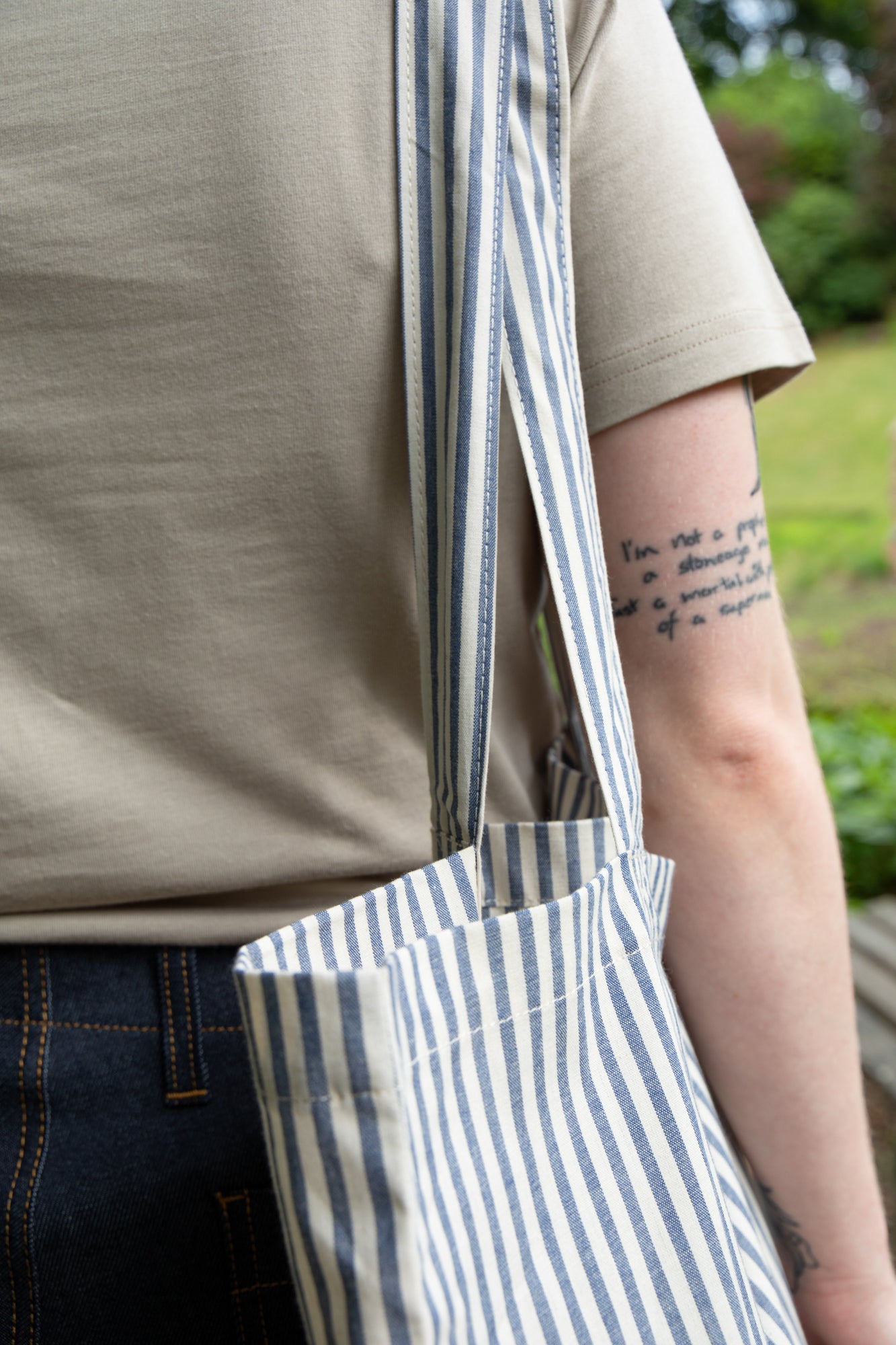 close up of the blue and white stripe tote bag over a ladies arm wearing short sleeve t shirt in stone and indigo jeans