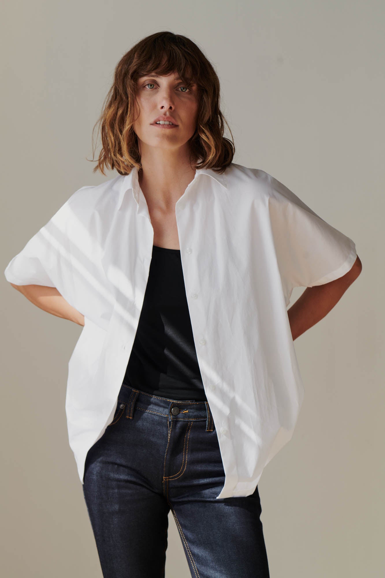 Female wearing Ava short sleeve shirt in white unbuttoned over black camisole 
