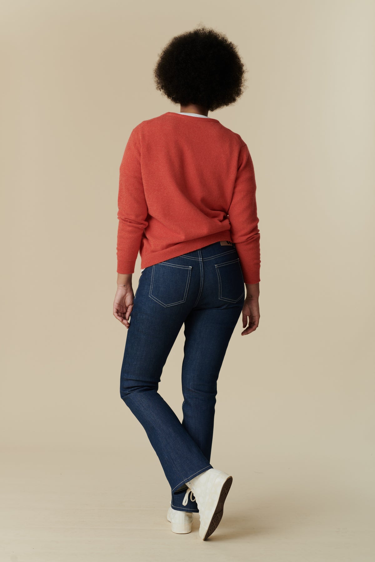 
            Full body back shot of black female model with afro wearing the women&#39;s bootcut mid rise jeans in blue paired with flame red, lambswool crew neck jumper