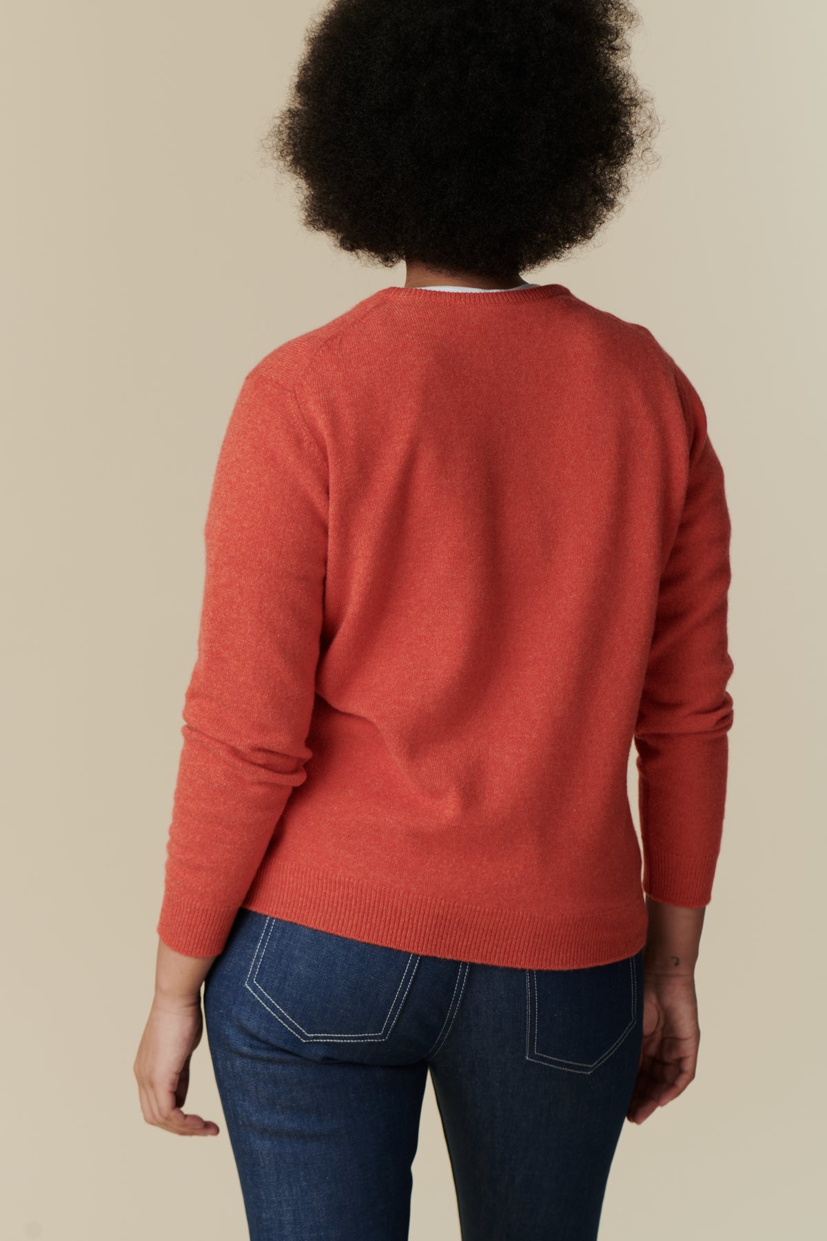 Thigh up back shot of black female model with dark brown afro hair wearing lambswool crew neck in flame red paired with women's bootcut mid rise jeans in blue