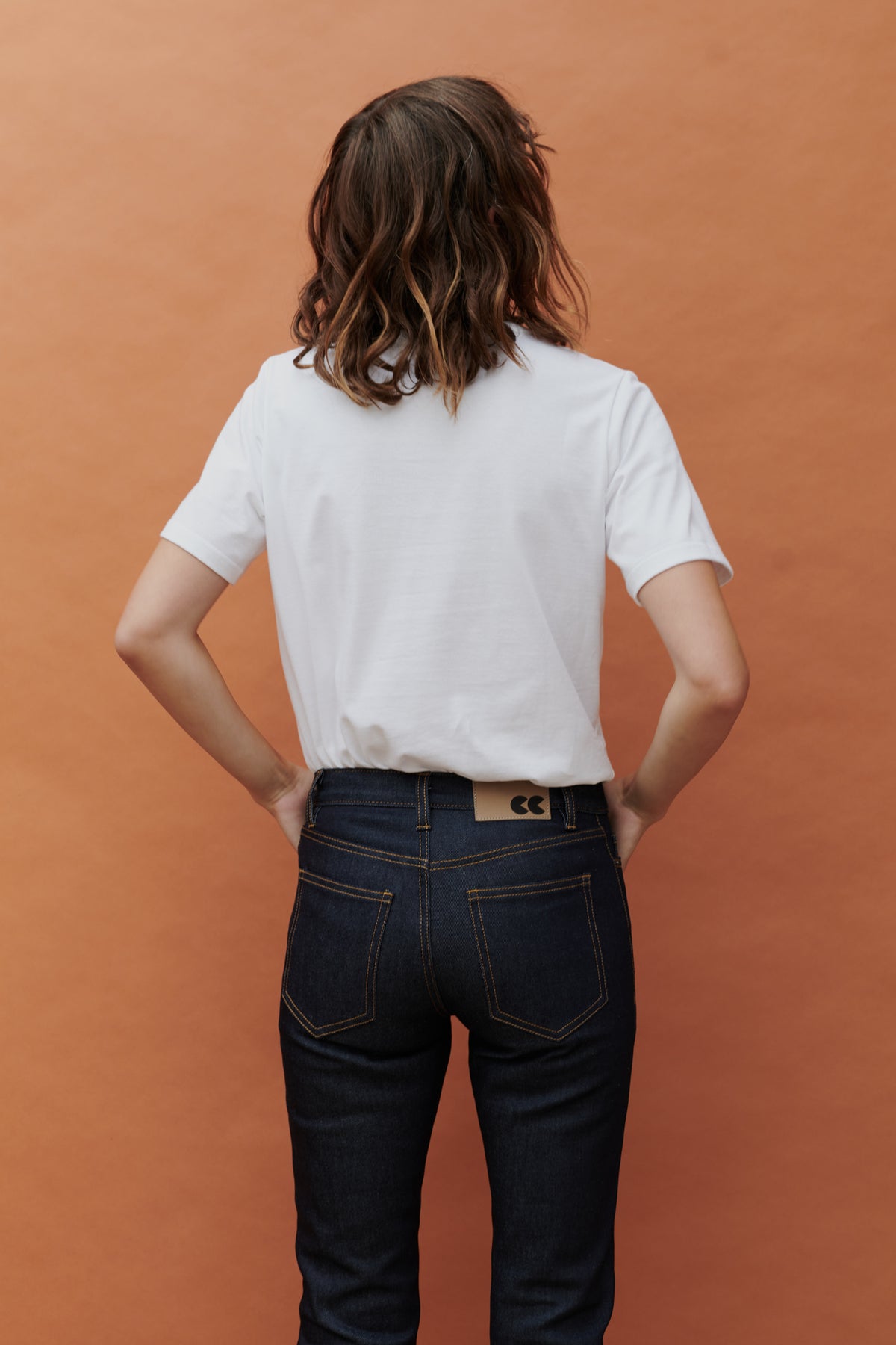 Back of female wearing mid rise straight leg jean in indigo. Back pocket and belt loop detail