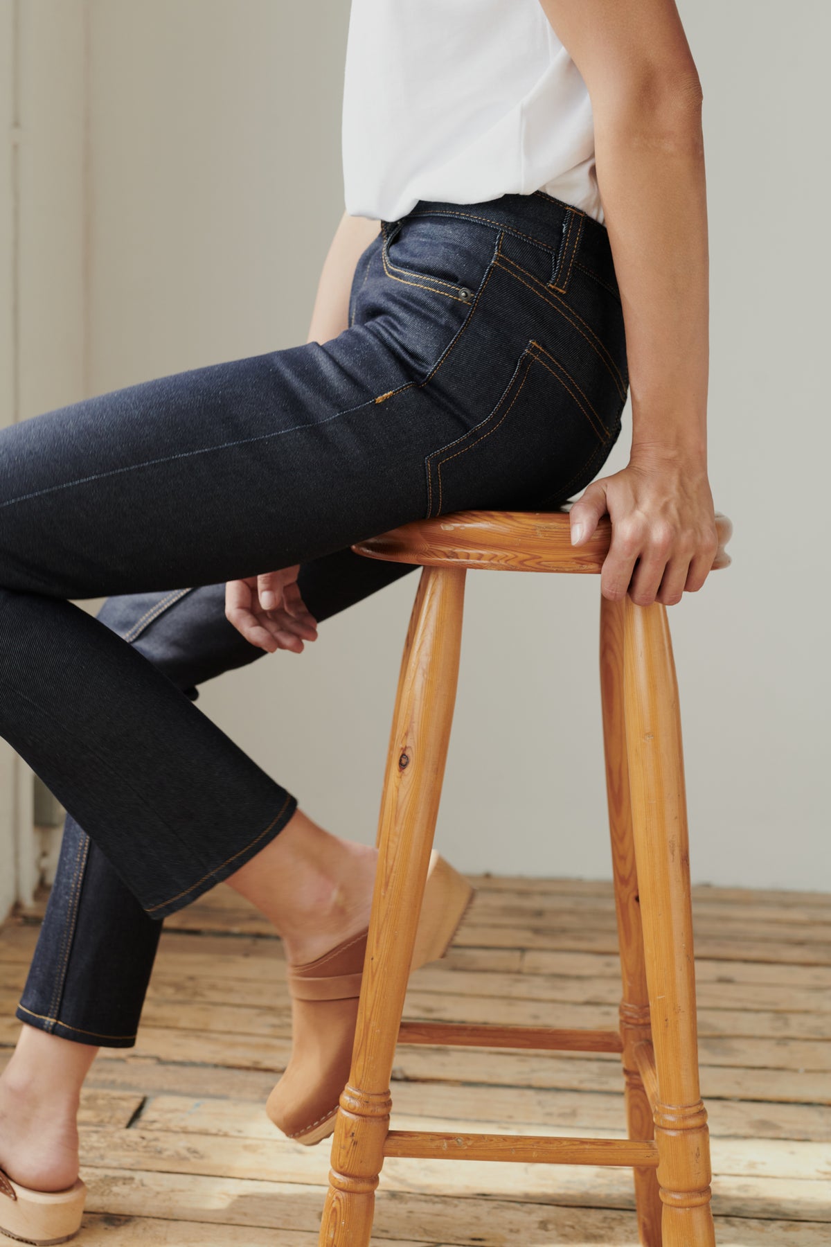 Side view of female sat on stool, wearing mid rise straight leg jean in indigo