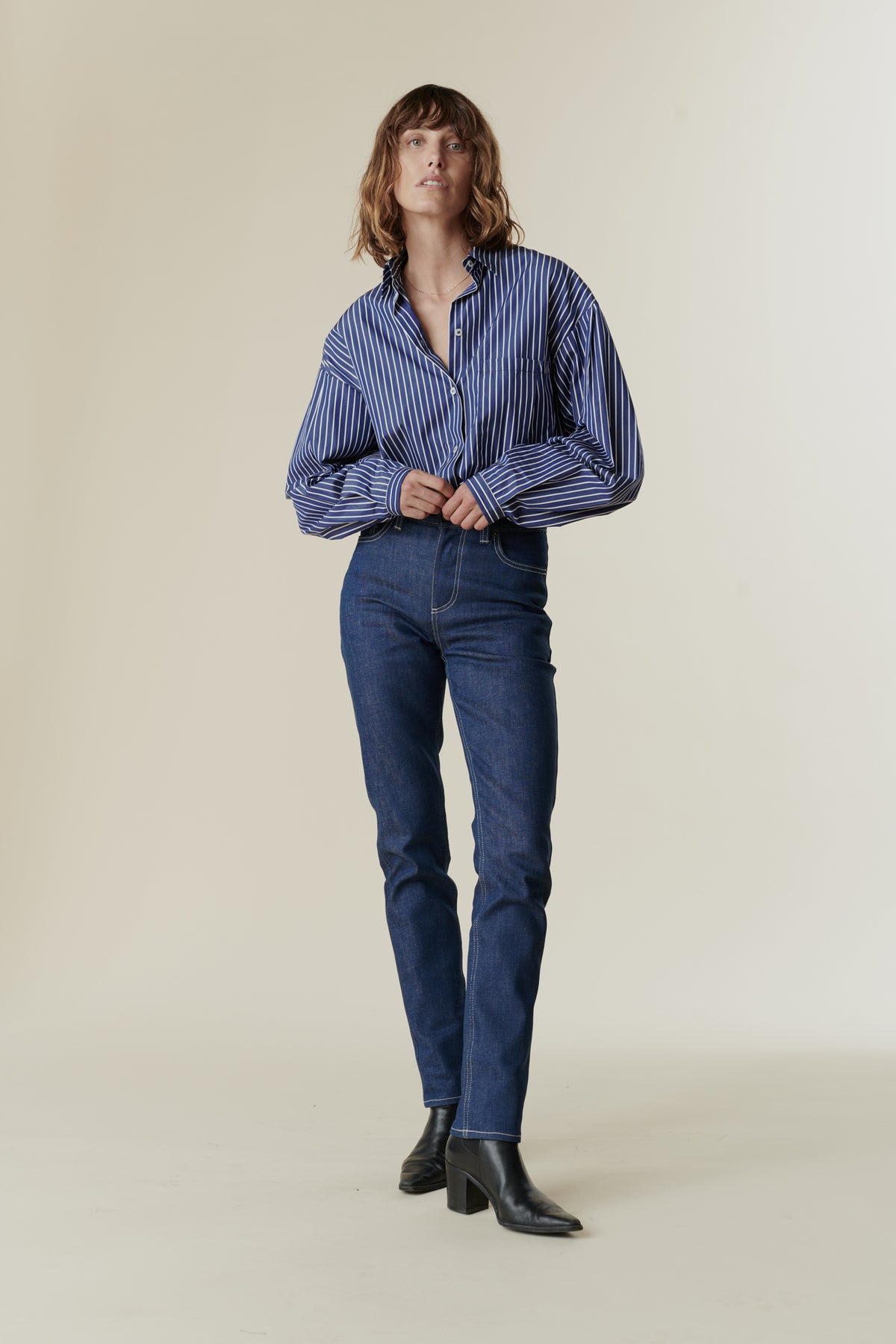 
            Front full body image female wearing straight leg high rise jean in blue paired with long sleeve Esme shirt in blue and white.