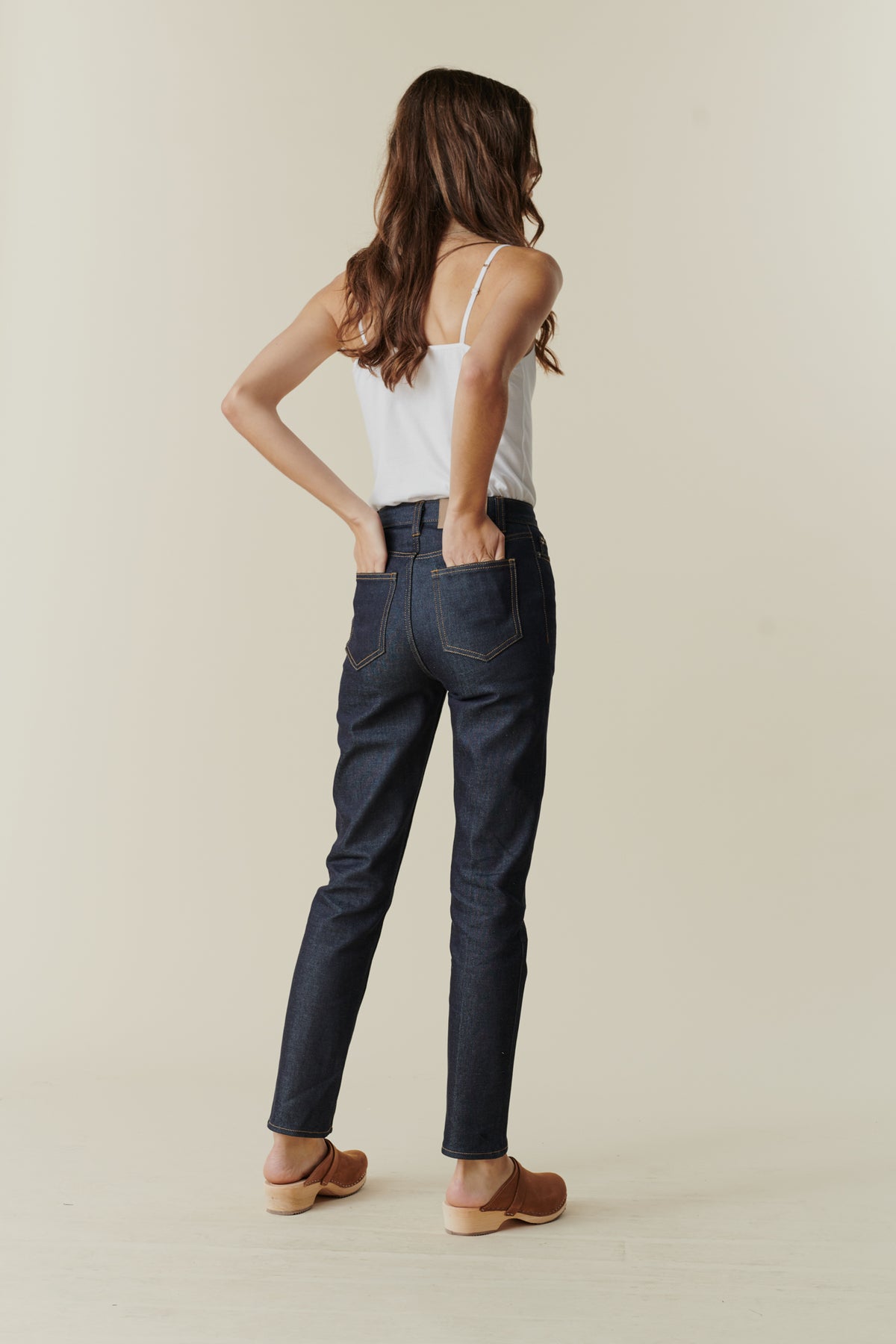 Full body image showing back of female wearing straight leg high rise jean in indigo with back pockets.