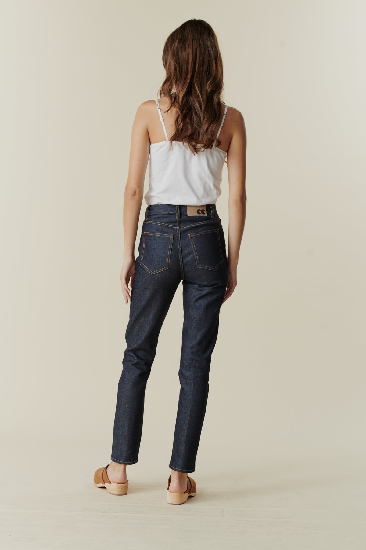 Full body image showing back of female wearing straight leg high rise jean in indigo.