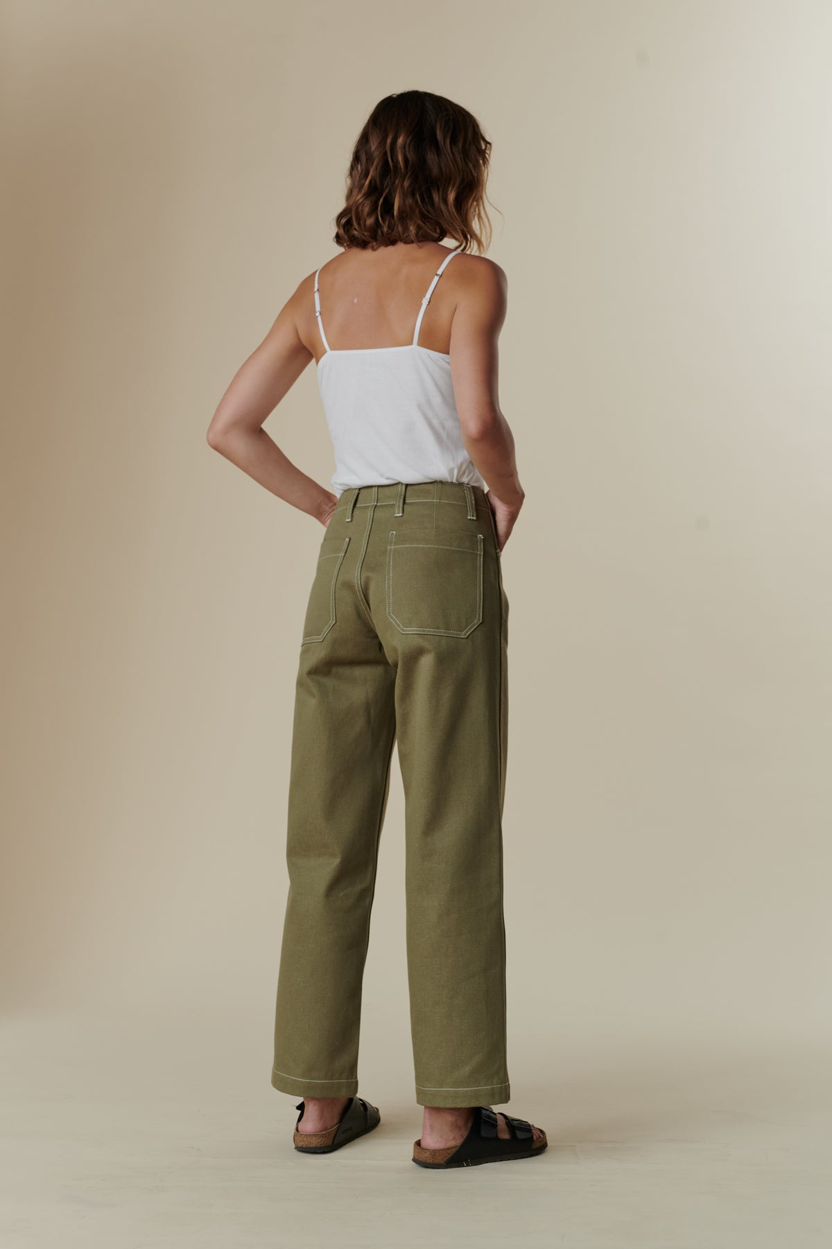 
            back frame of female wearing olive work jean with white vest top and birkenstock sandals