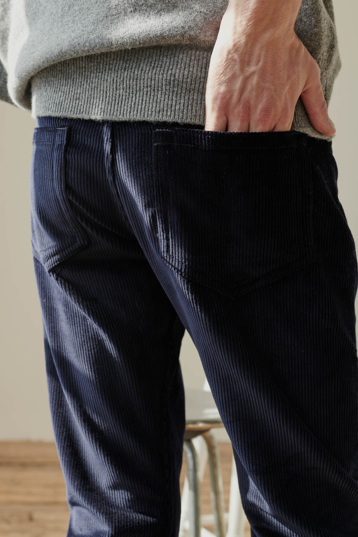 Shot of white male with hand in back pocket of men's five pocket cord trousers in navy. Worn with grey lambswool crew neck jumper