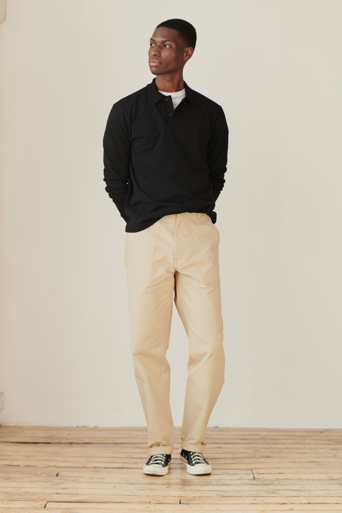 Full body image of man wearing black long sleeve polo shirt layered over white t-shirt and paired with combat pant in putty