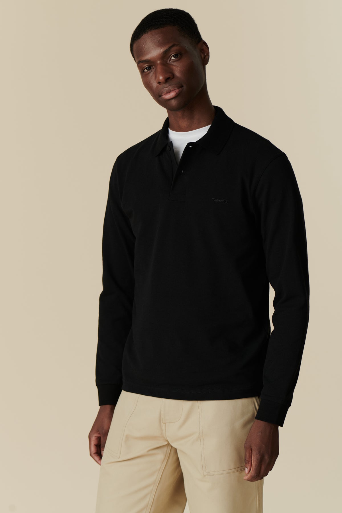 man wearing white t-shirt underneath a black long sleeve community clothing polo shirt with combat pants in putty