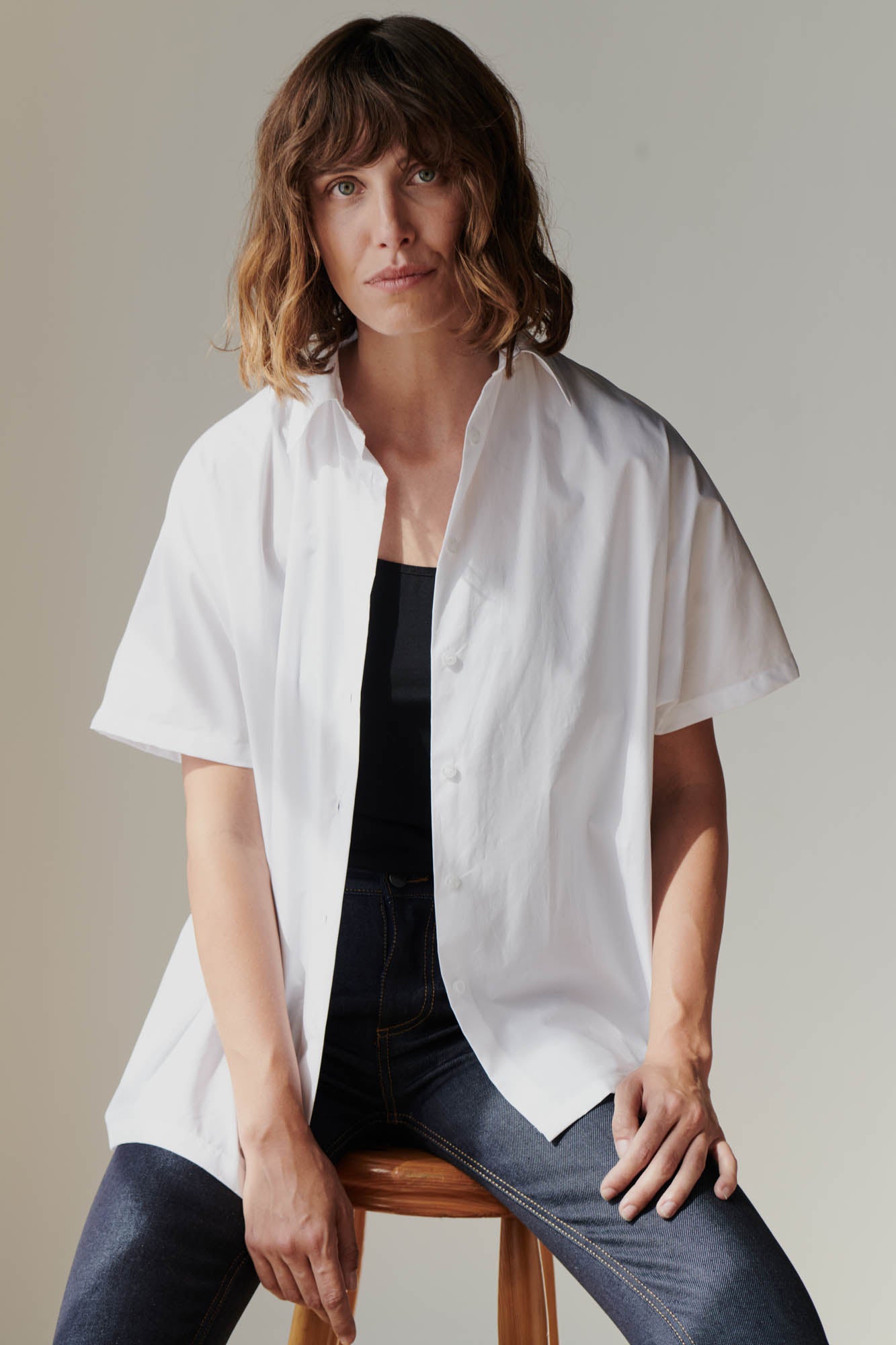 Portrait of female wearing Ava short sleeve shirt in white unbuttoned over black camisole 