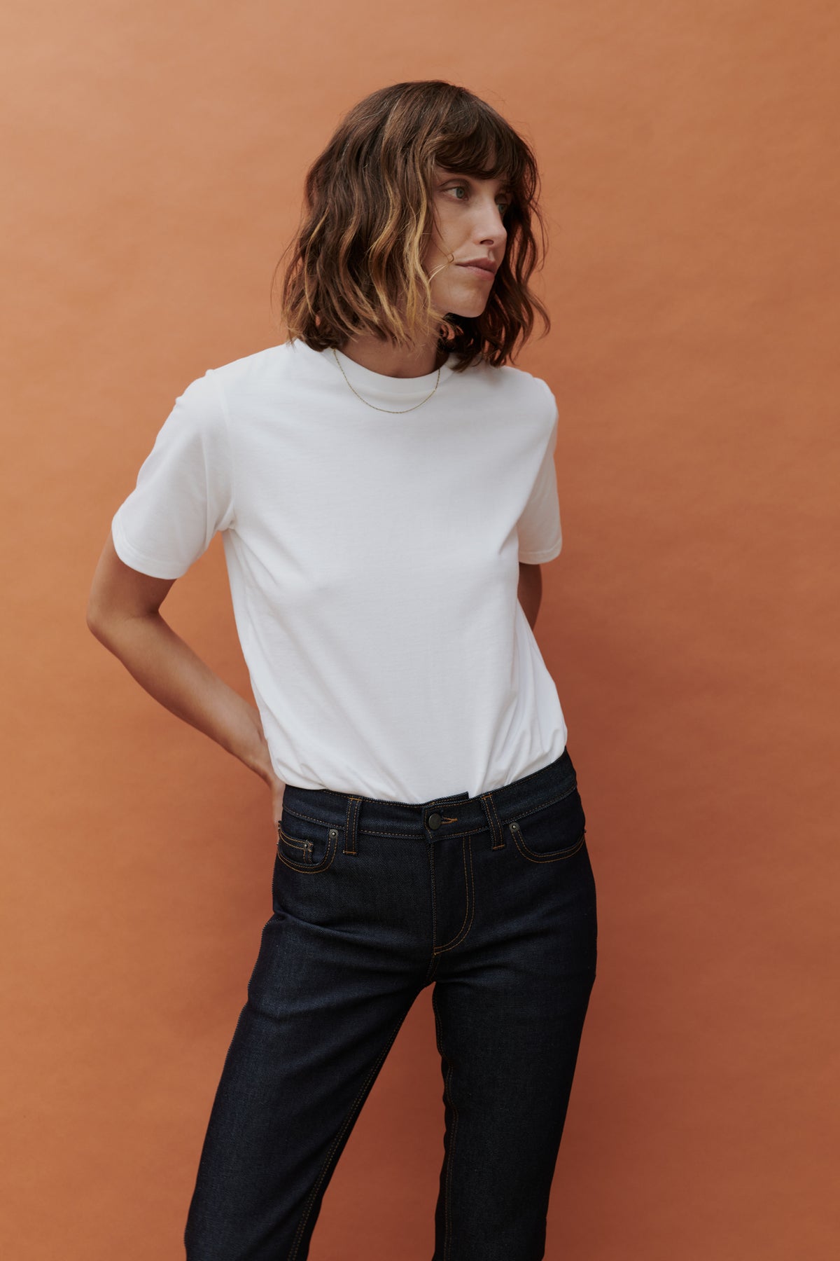 Image of brunette female wearing white t shirt tucked into mid rise straight leg jean