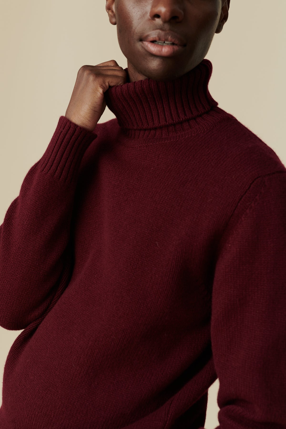 
            Black male wearing lambswool roll neck in burgundy. Detail image of ribbed roll neck and cuff.